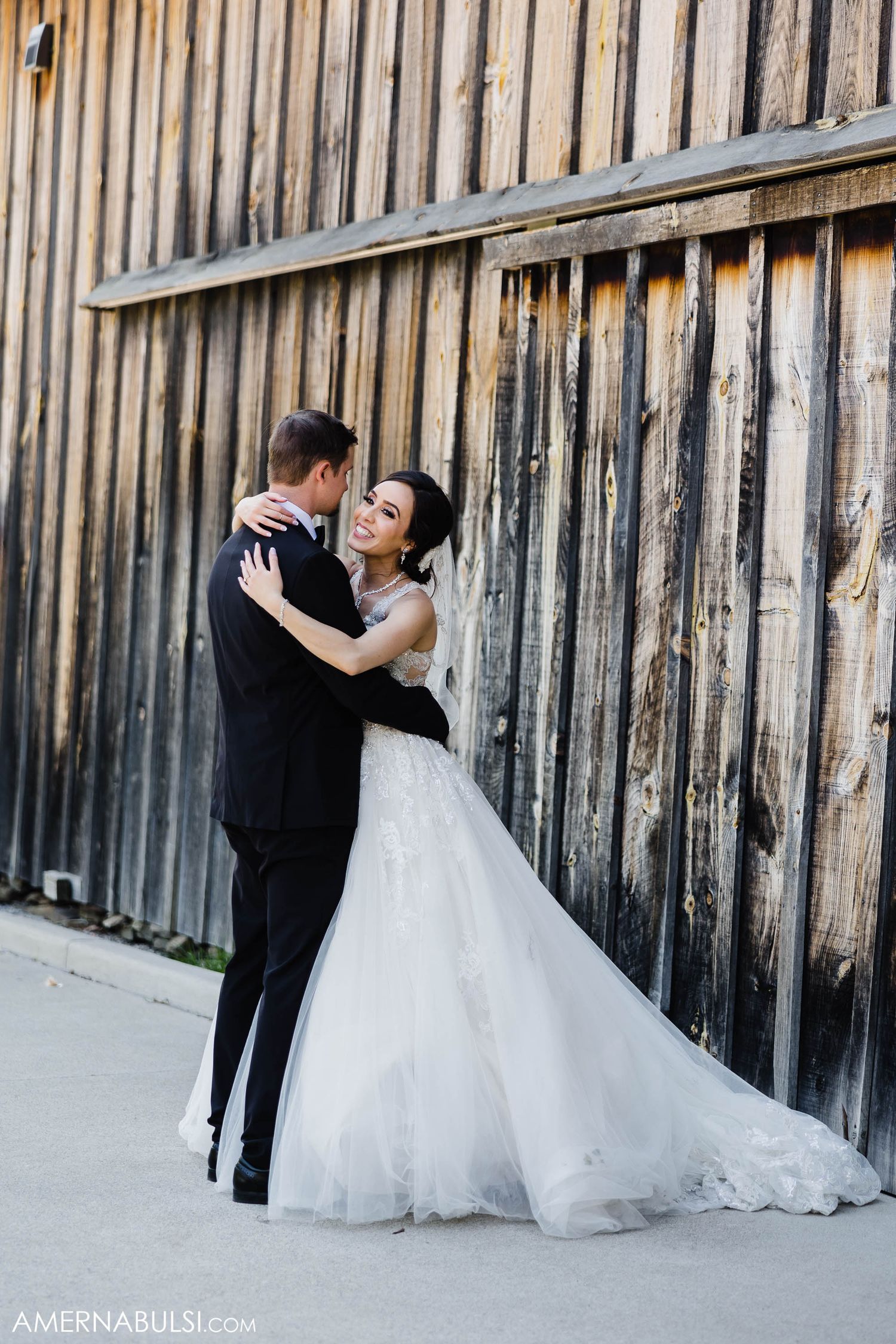 Full-length shot of newlyweds embracing against weathered wooden wall background.