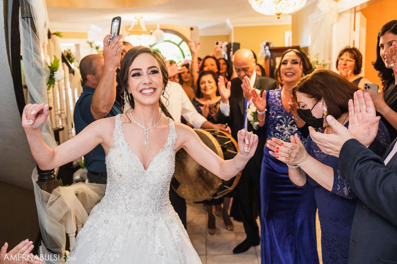 A joyful celebration at a wedding reception with guests clapping and dancing in an indoor venue.
