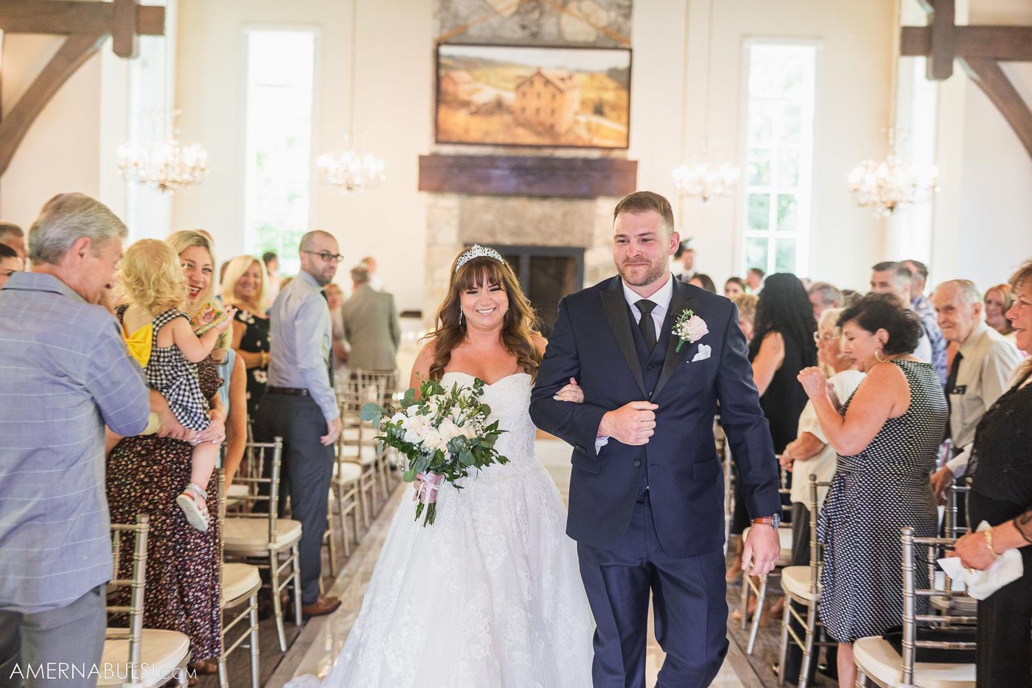 Newlyweds walk down church aisle after ceremony while guests applaud from white chairs.
