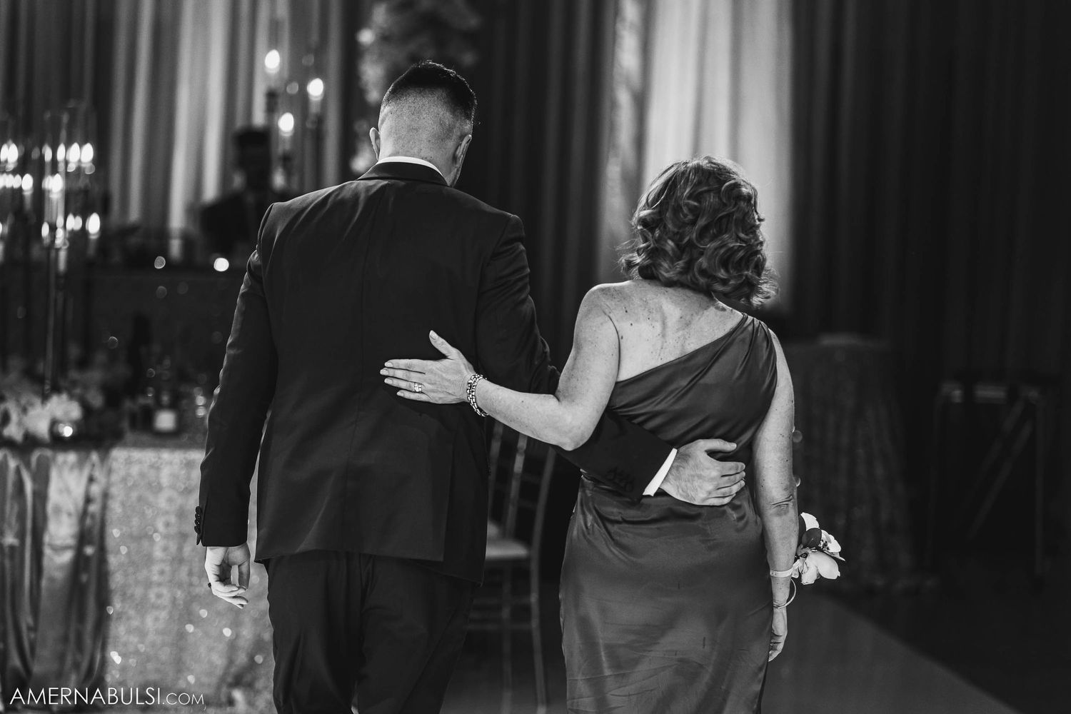 Black and white photo of couple walking arm in arm during their wedding reception.