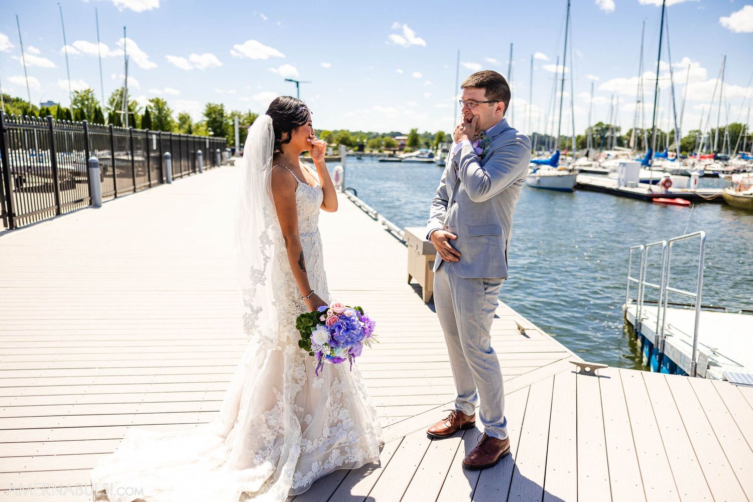 Wedding couple shares an emotional moment on a marina boardwalk with sailboats in the background.