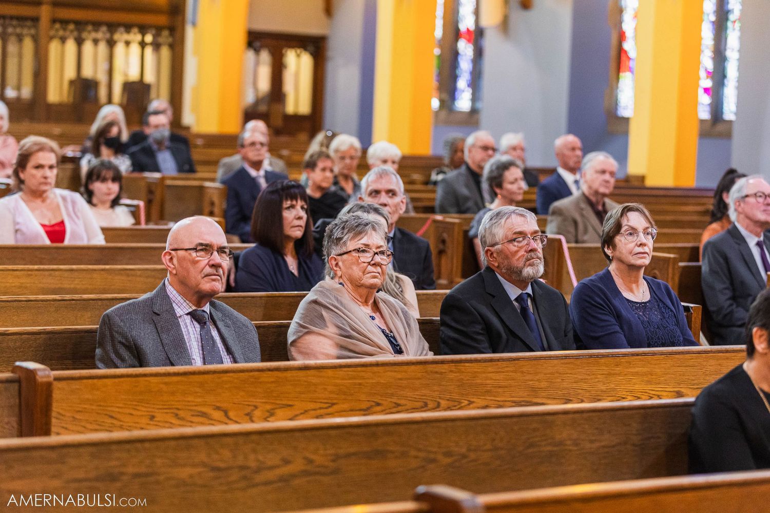 Wedding guests seated in wooden church pews during ceremony.