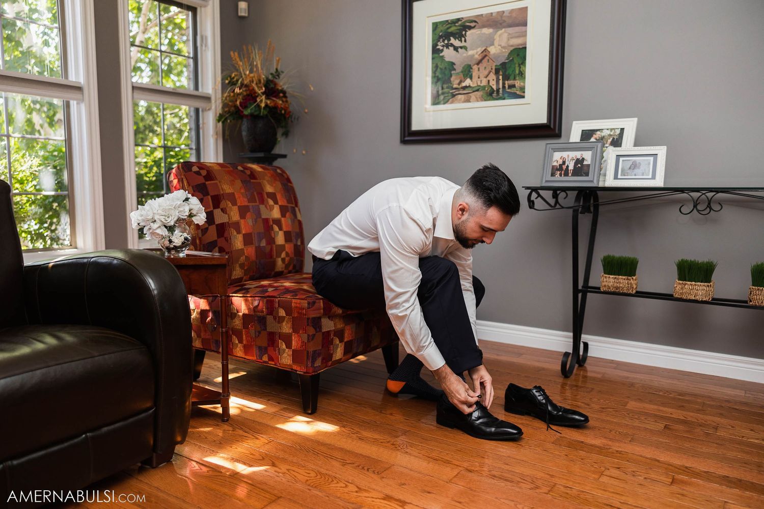Person putting on formal shoes while sitting in living room with hardwood floors.