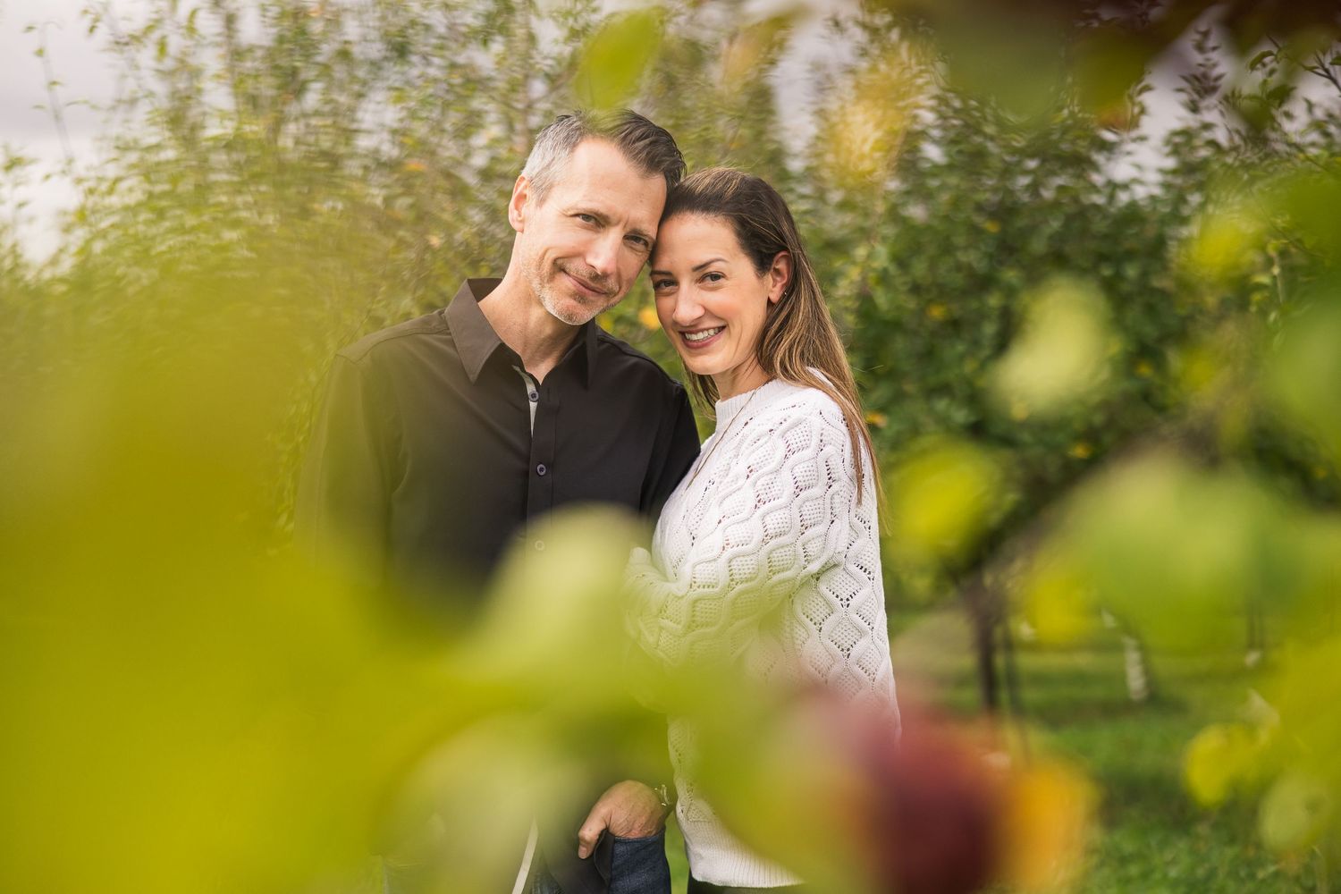 A happy couple embraces and laughs together in a lush green outdoor setting during an autumn photo session.