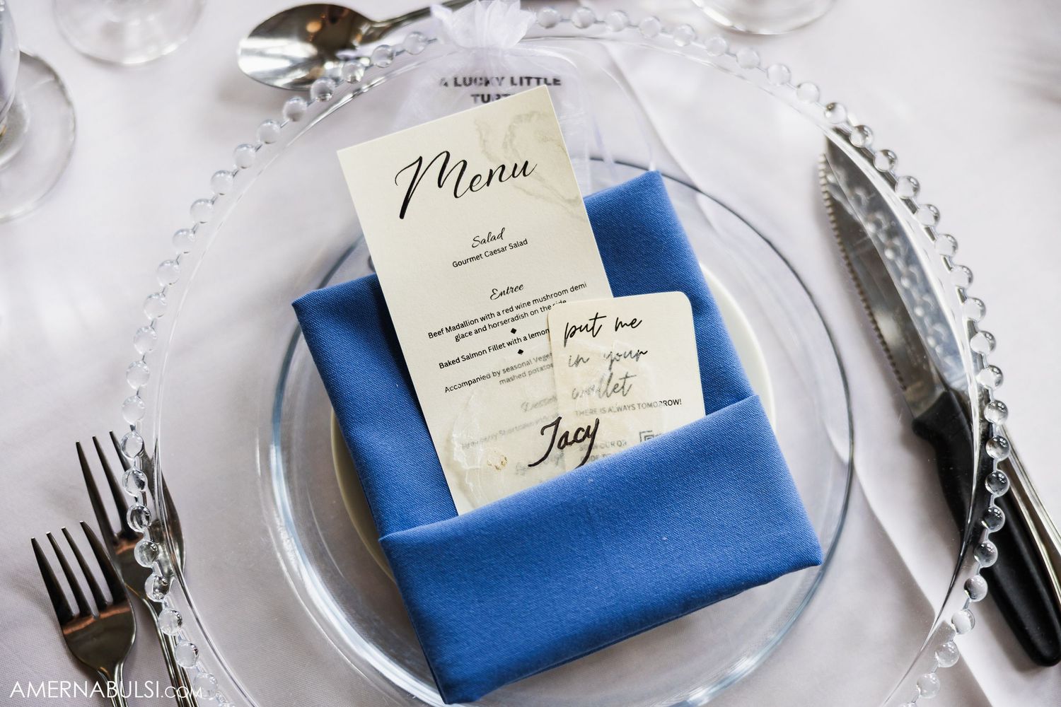 Elegant place settings with blue napkins and printed menu cards at wedding reception.