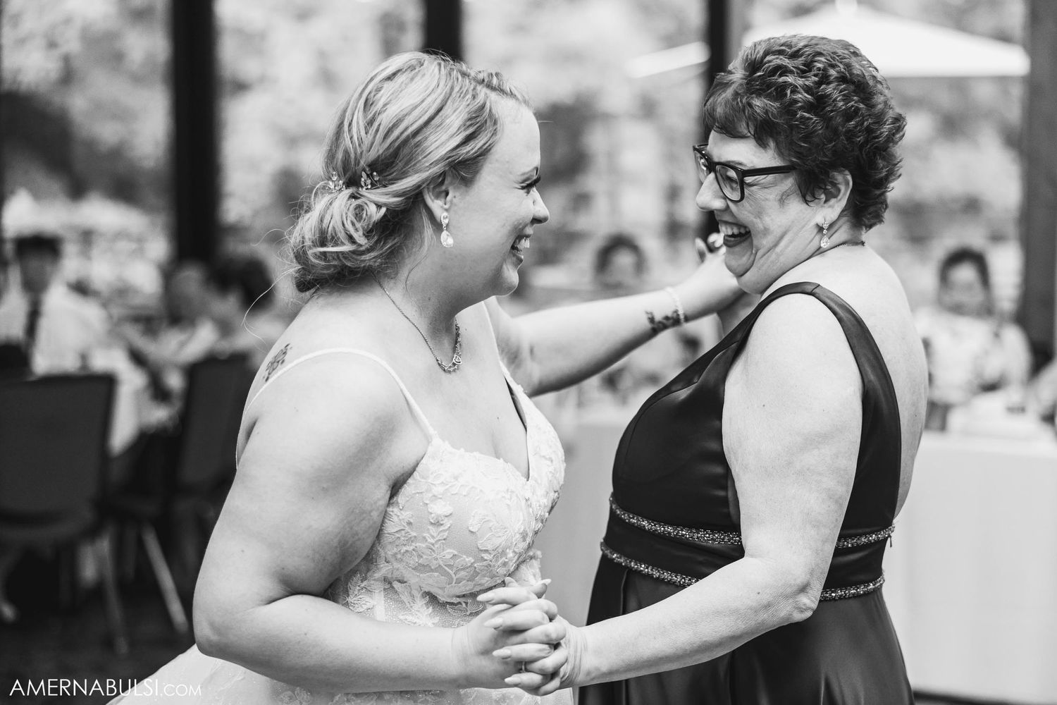 A touching moment between two wedding attendees sharing a joyful embrace and laughter in black and white.