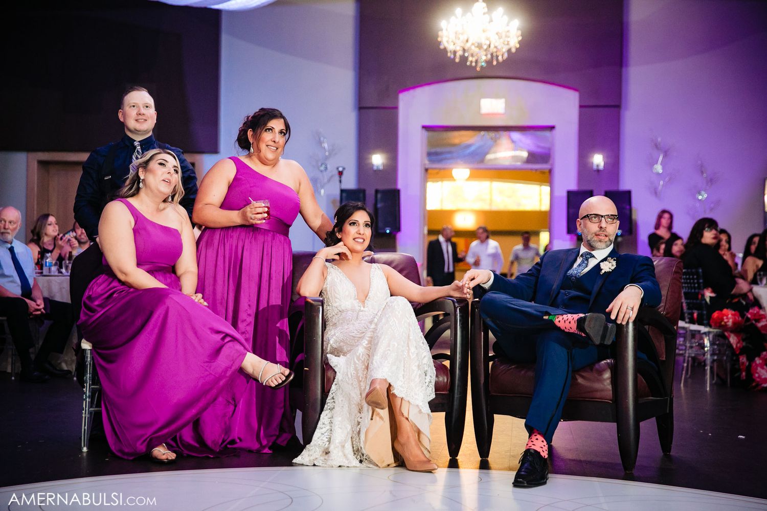 Wedding guests dance and celebrate on a purple-lit dance floor during an elegant reception celebration.