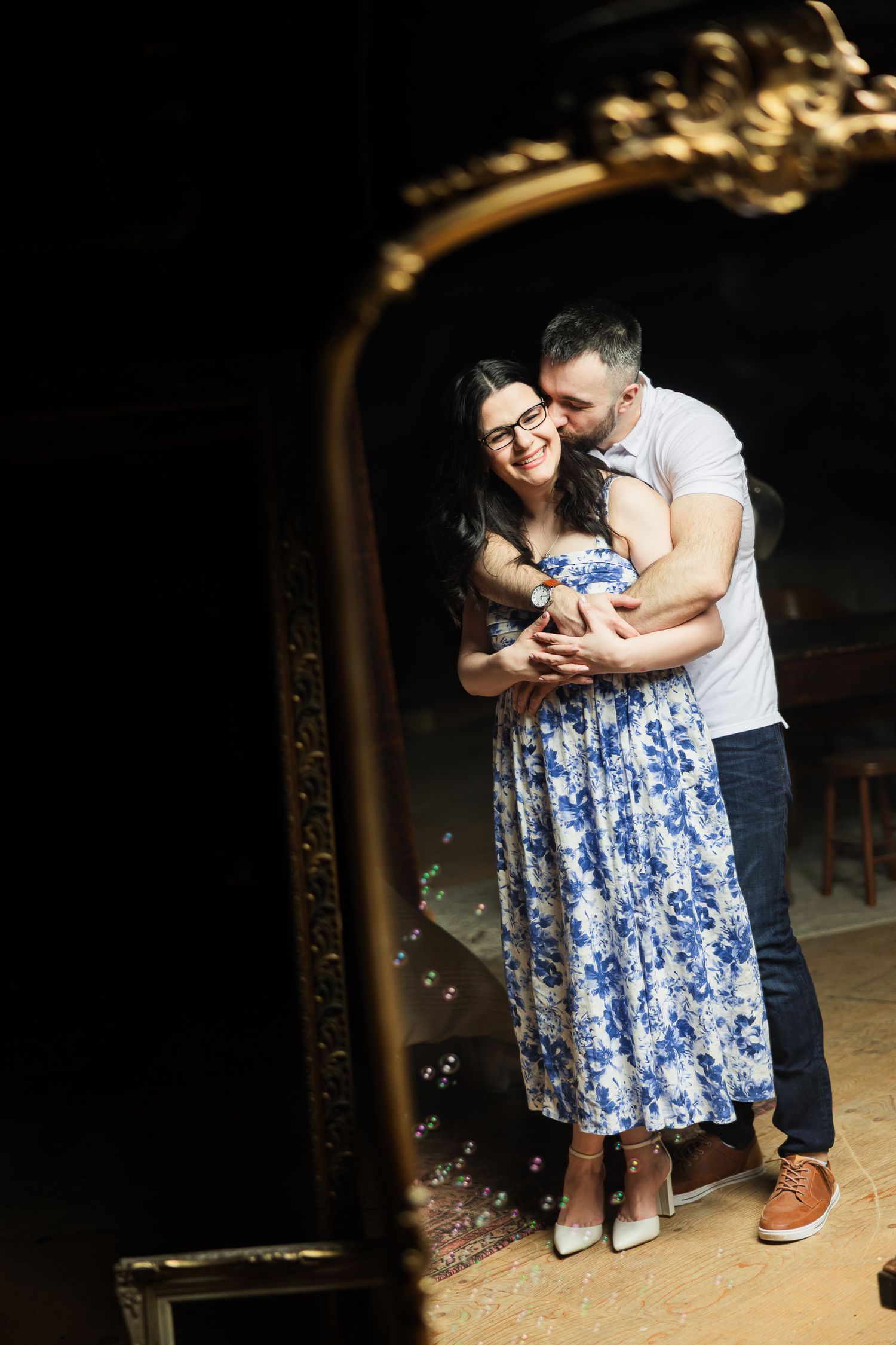 A couple shares an intimate moment with their newborn baby seen through an ornate vintage mirror.