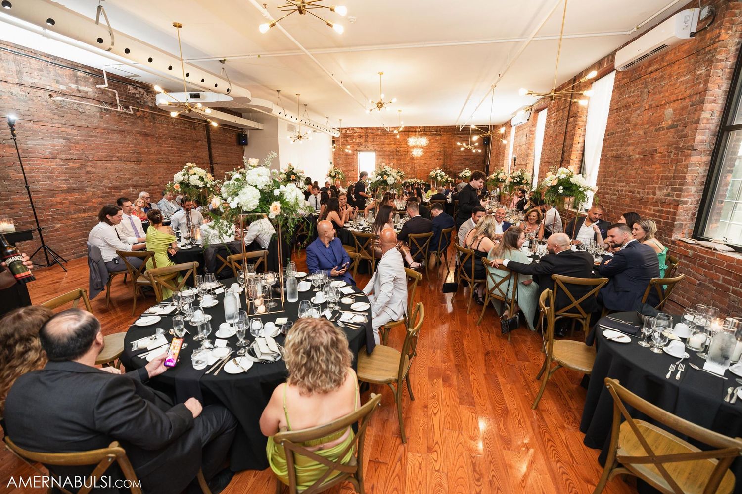 Wedding reception dinner setup in rustic venue with exposed brick and elegant table settings.