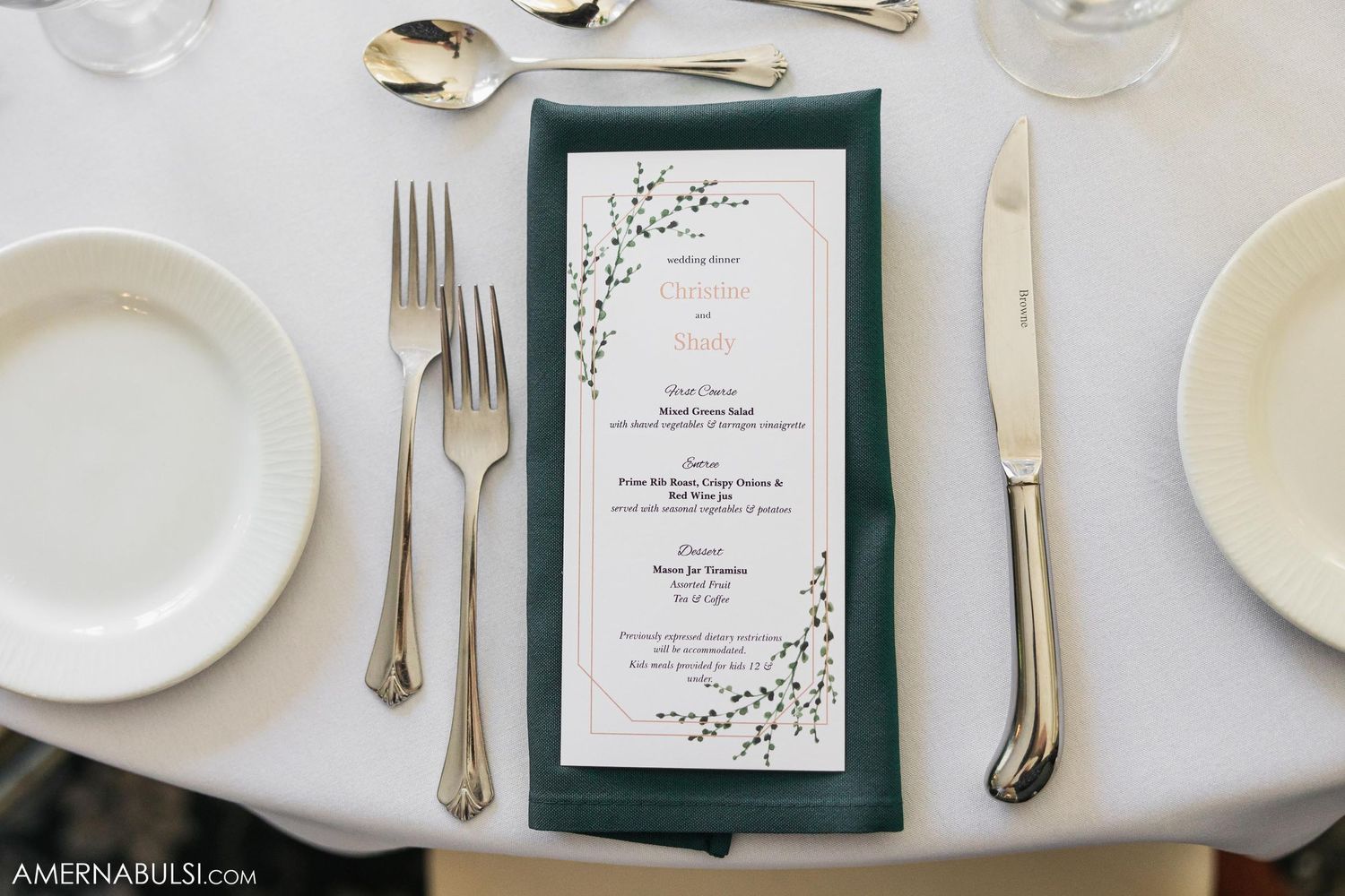 An elegant place setting featuring a dark green menu card with floral design and silver cutlery.