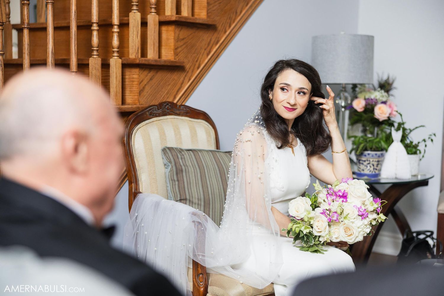 Bride seated indoors holding bouquet during wedding preparations.