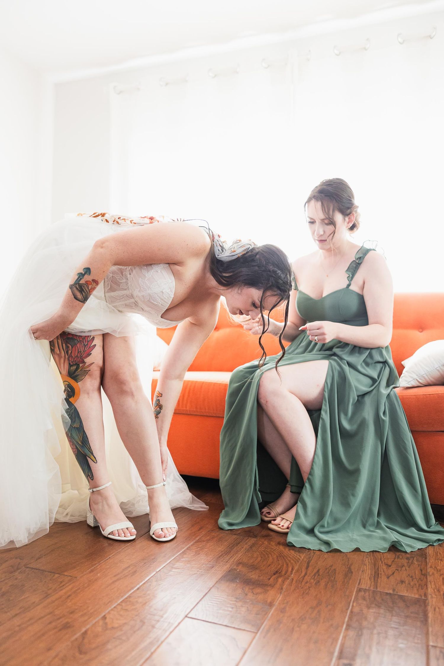 Wedding preparation scene with bride and bridesmaid on orange couch.