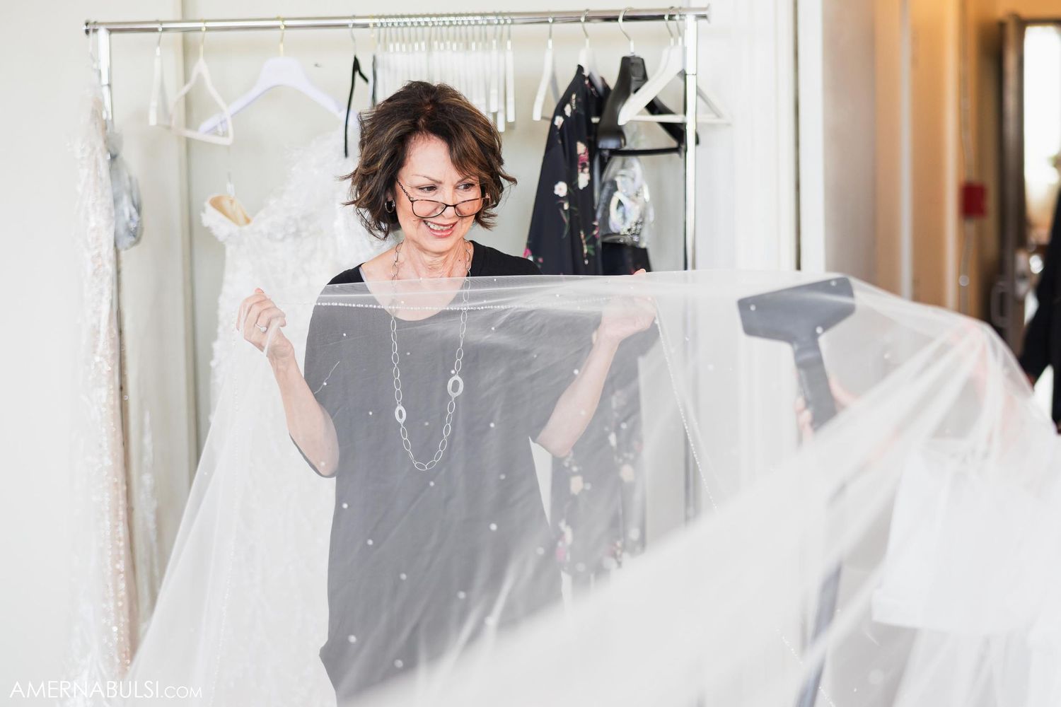Woman holds sheer wedding veil in bridal preparation room.
