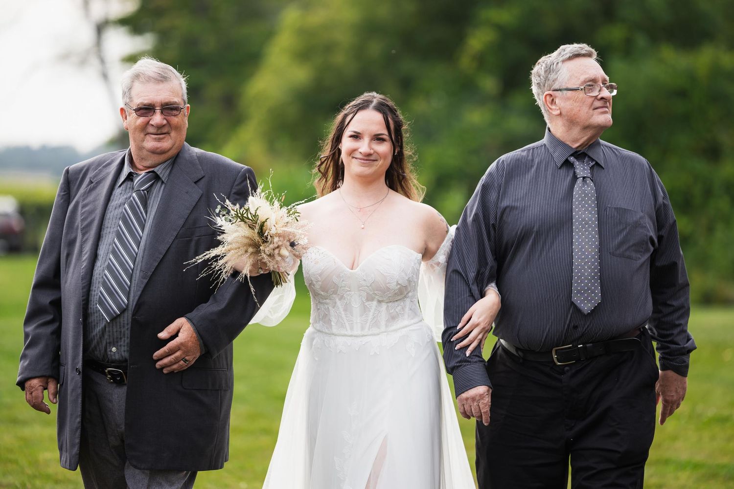 Bride in white dress walks down aisle escorted by two men in dark suits.