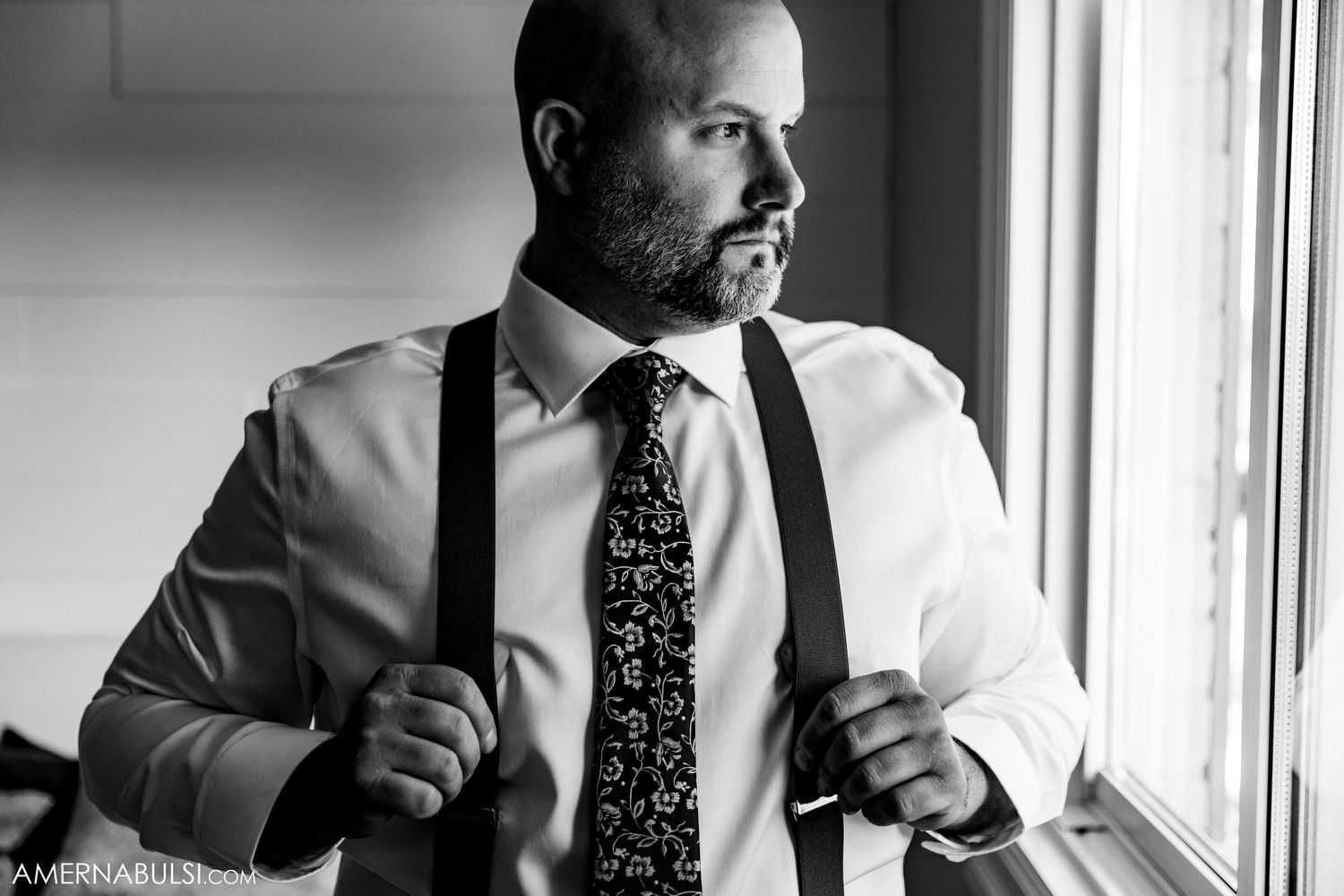 Black and white portrait of person adjusting tie by window.