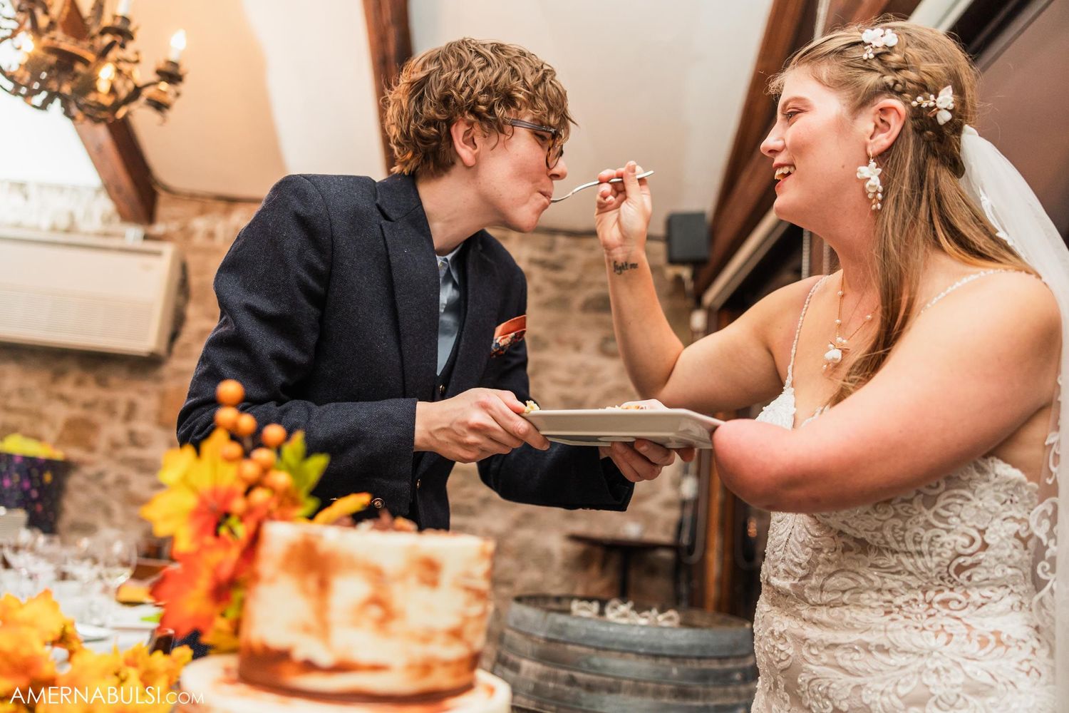 Playful moment during wedding reception with cake tasting in rustic indoor setting.