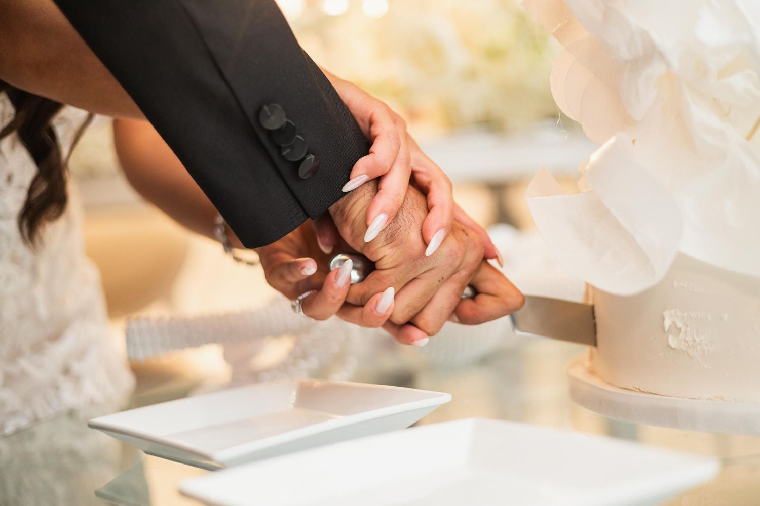 Close-up of hands cutting wedding cake together at elegant reception.