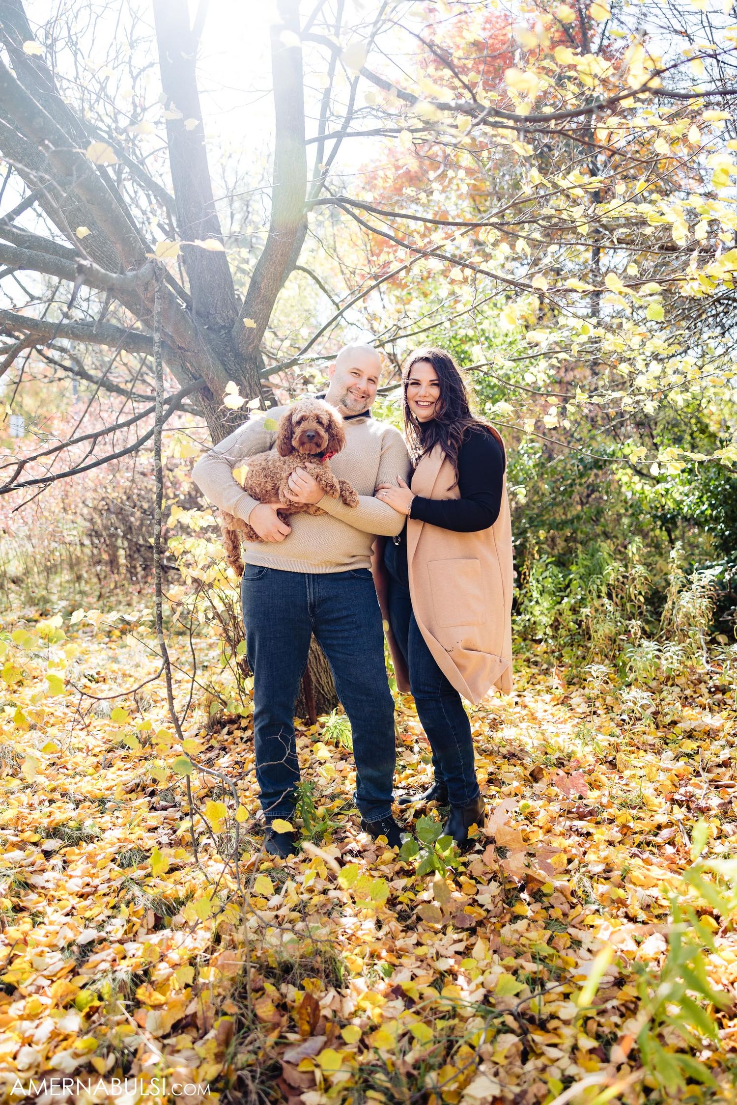 Couple holding their goldendoodle puppy amid fallen autumn leaves.