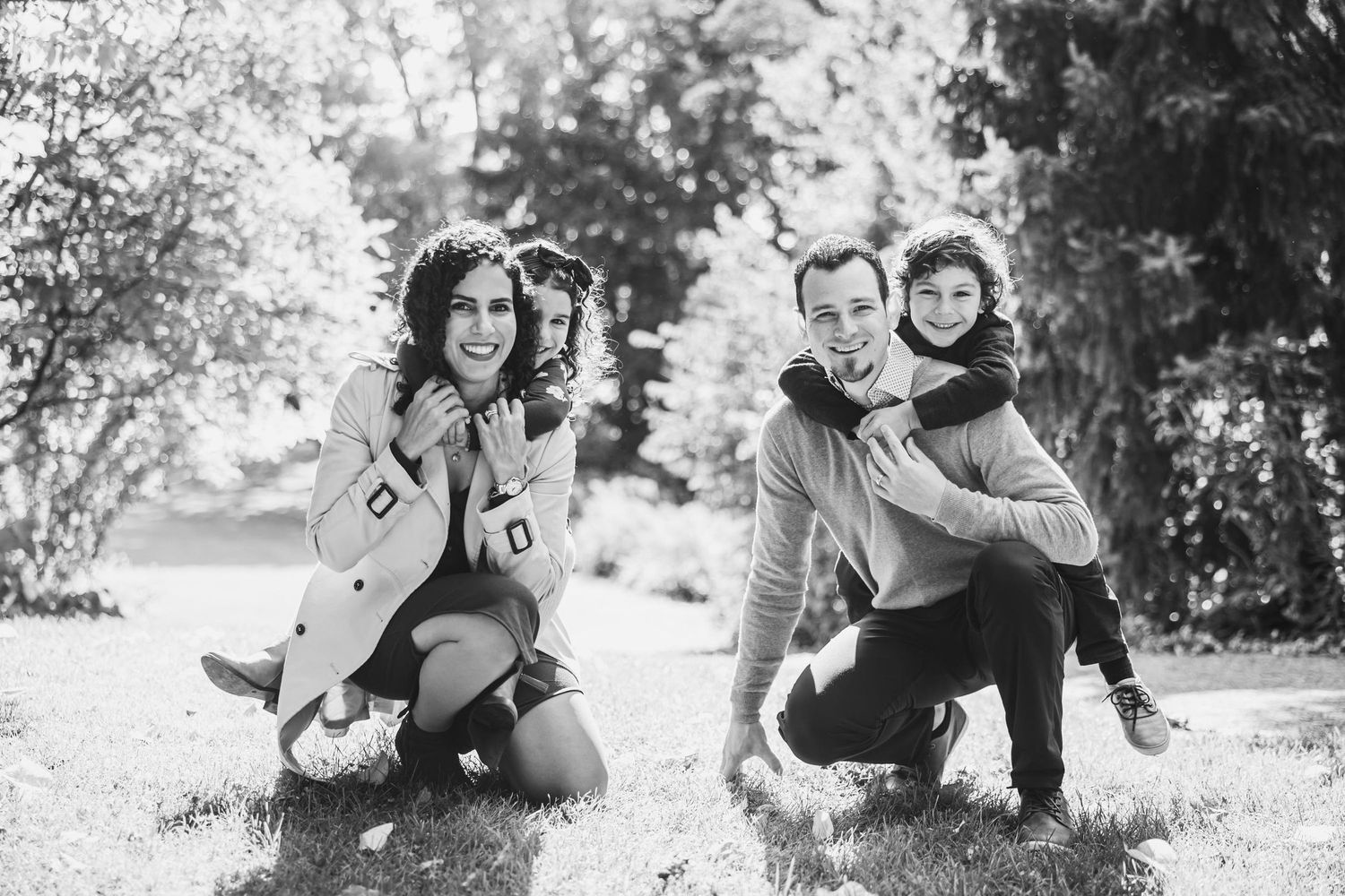 Two couples pose playfully on grass in black and white photography.
