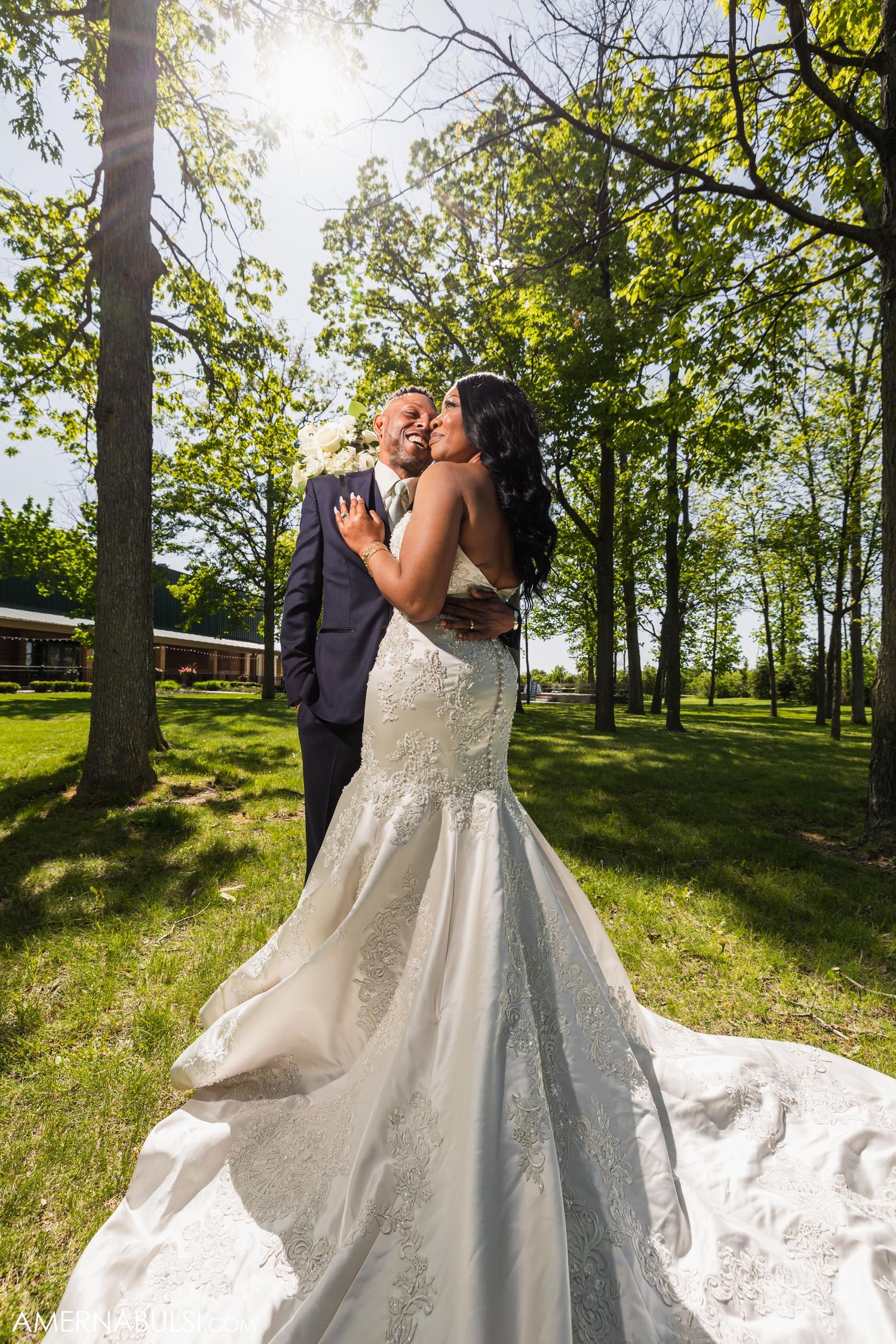 Romantic outdoor wedding portrait with bride's flowing dress train against natural forest backdrop.