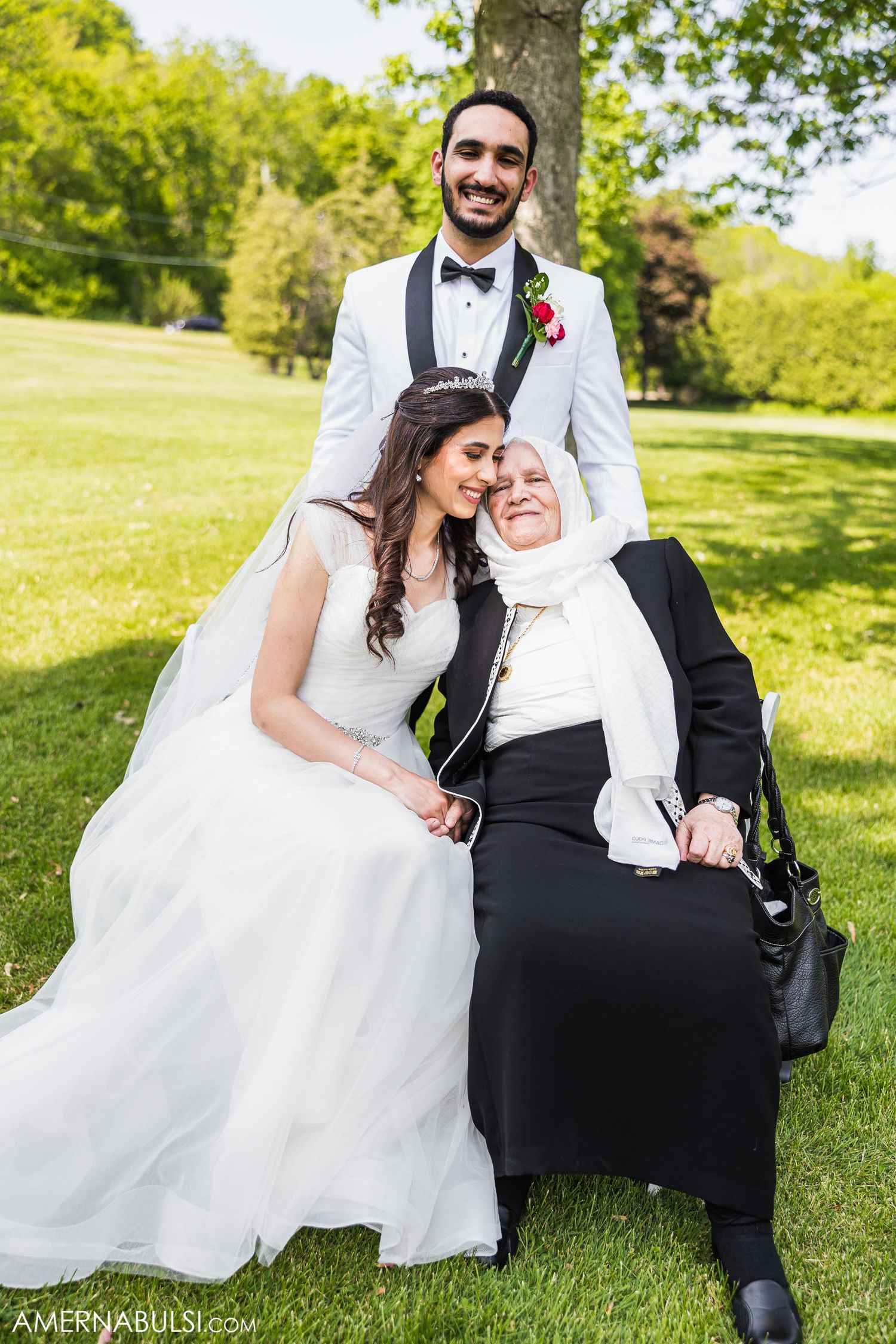 Wedding couple shares a tender moment outdoors with an elderly guest.