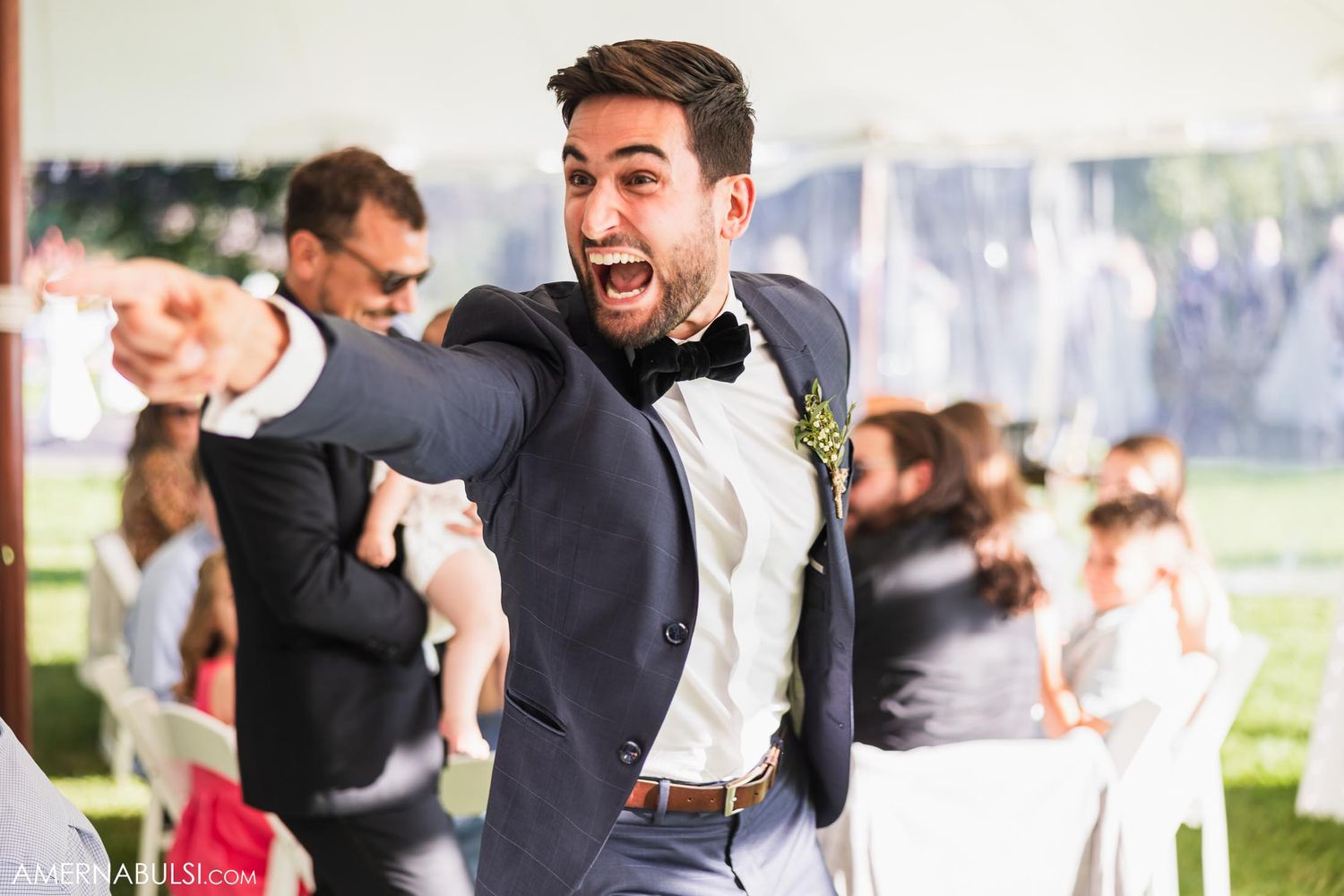 Excited wedding guest in navy suit and bowtie dancing enthusiastically at reception.