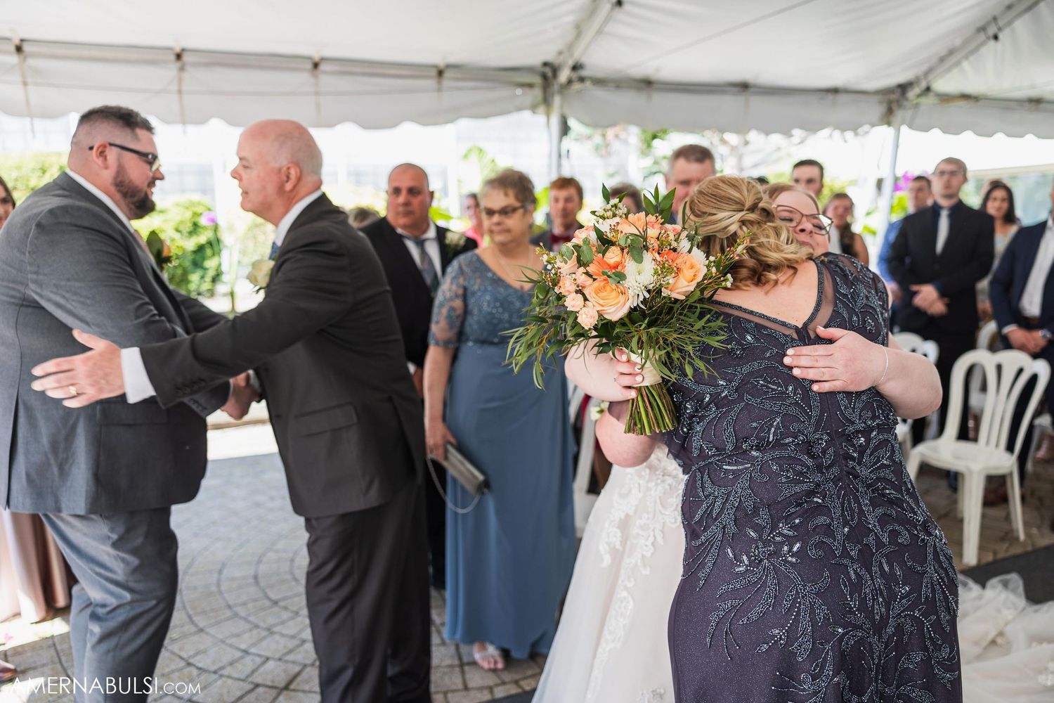 Wedding guests greeting each other during a celebration under a white tent.