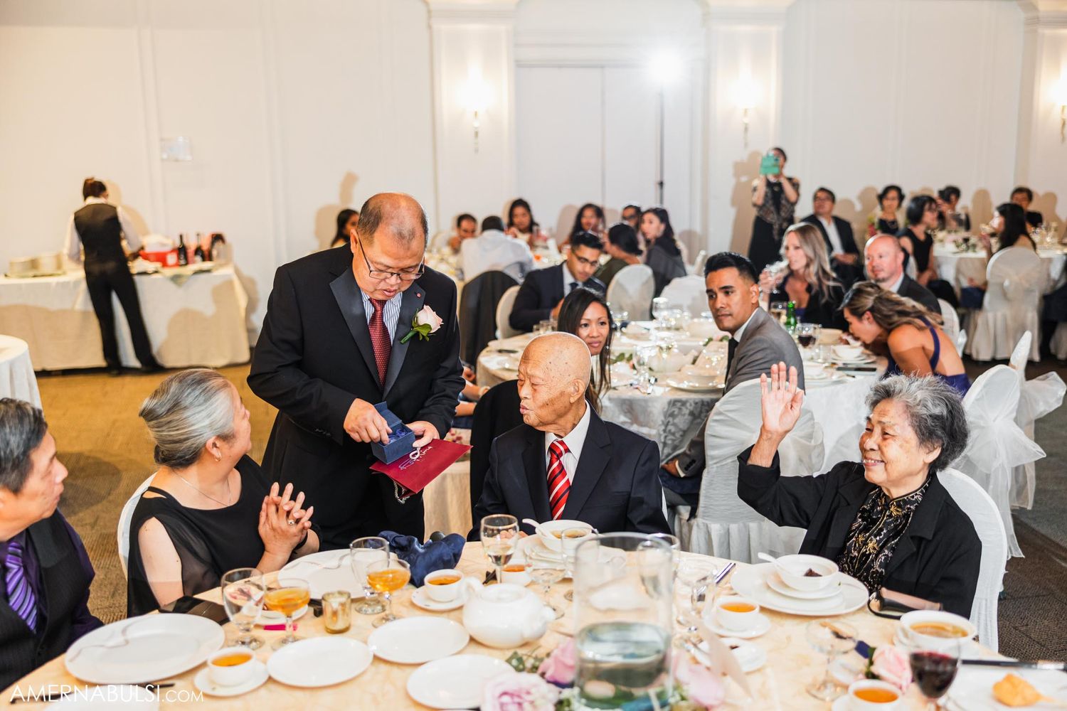 Wedding reception guests enjoy a formal dinner with table service in an elegantly decorated banquet hall.