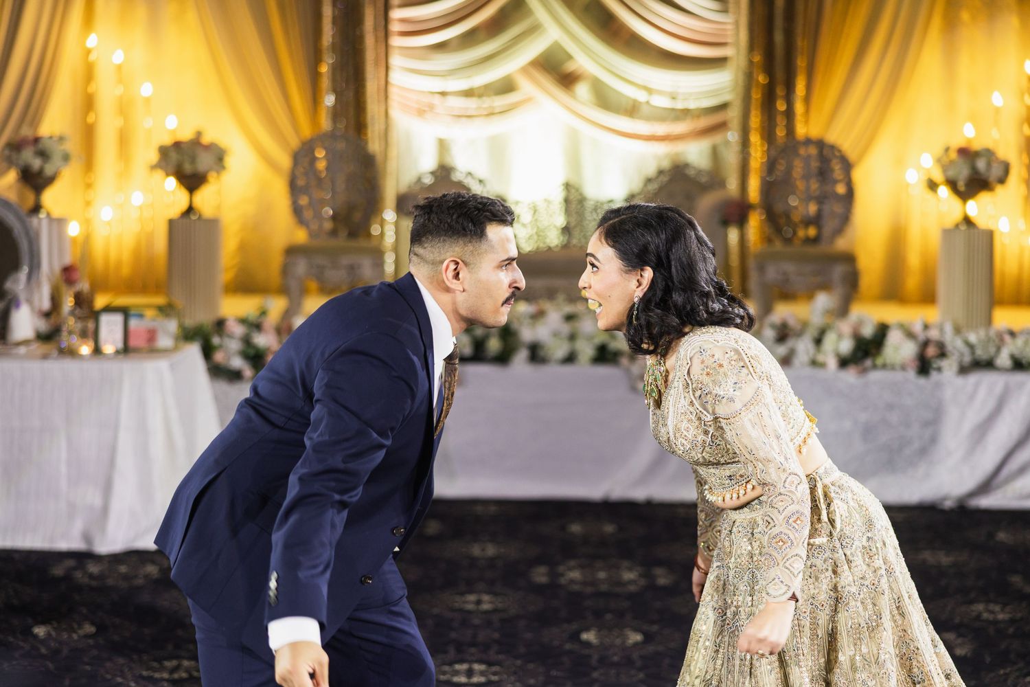 A couple in formal wedding attire shares a romantic moment in an elegant ballroom setting with golden decor.