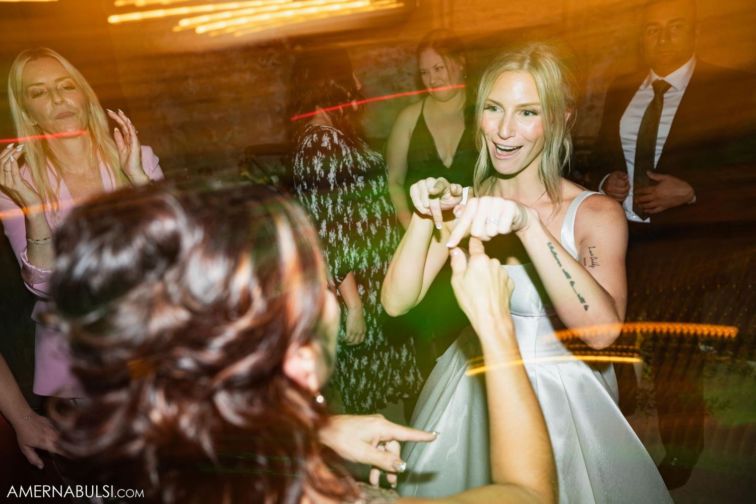 Wedding reception celebration with guests dancing in warm indoor lighting.