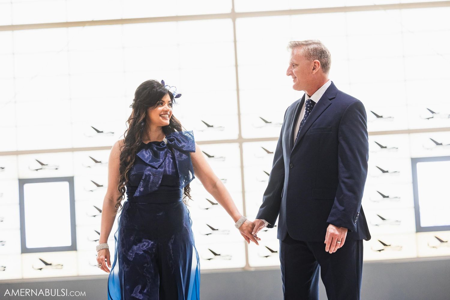 Elegant couple in formal attire standing by window with decorative bird silhouettes.