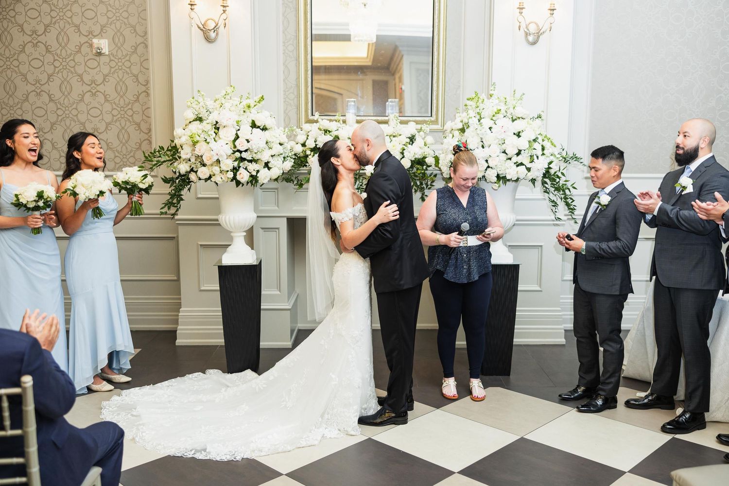 Wedding ceremony in elegant venue with white floral decorations and black and white checkered floor.