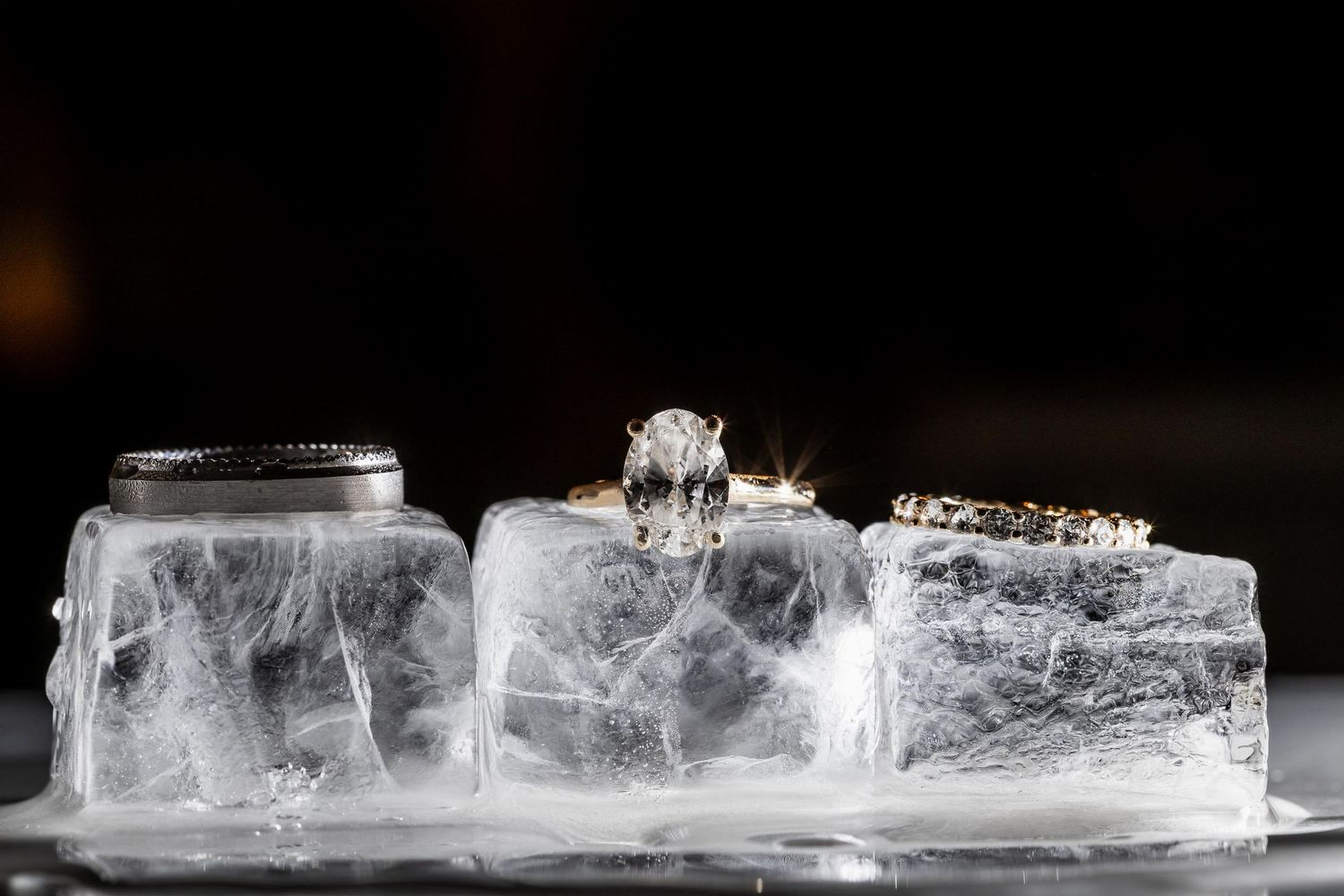Three frosted glass jars with jewelry displayed on ice in dramatic lighting.
