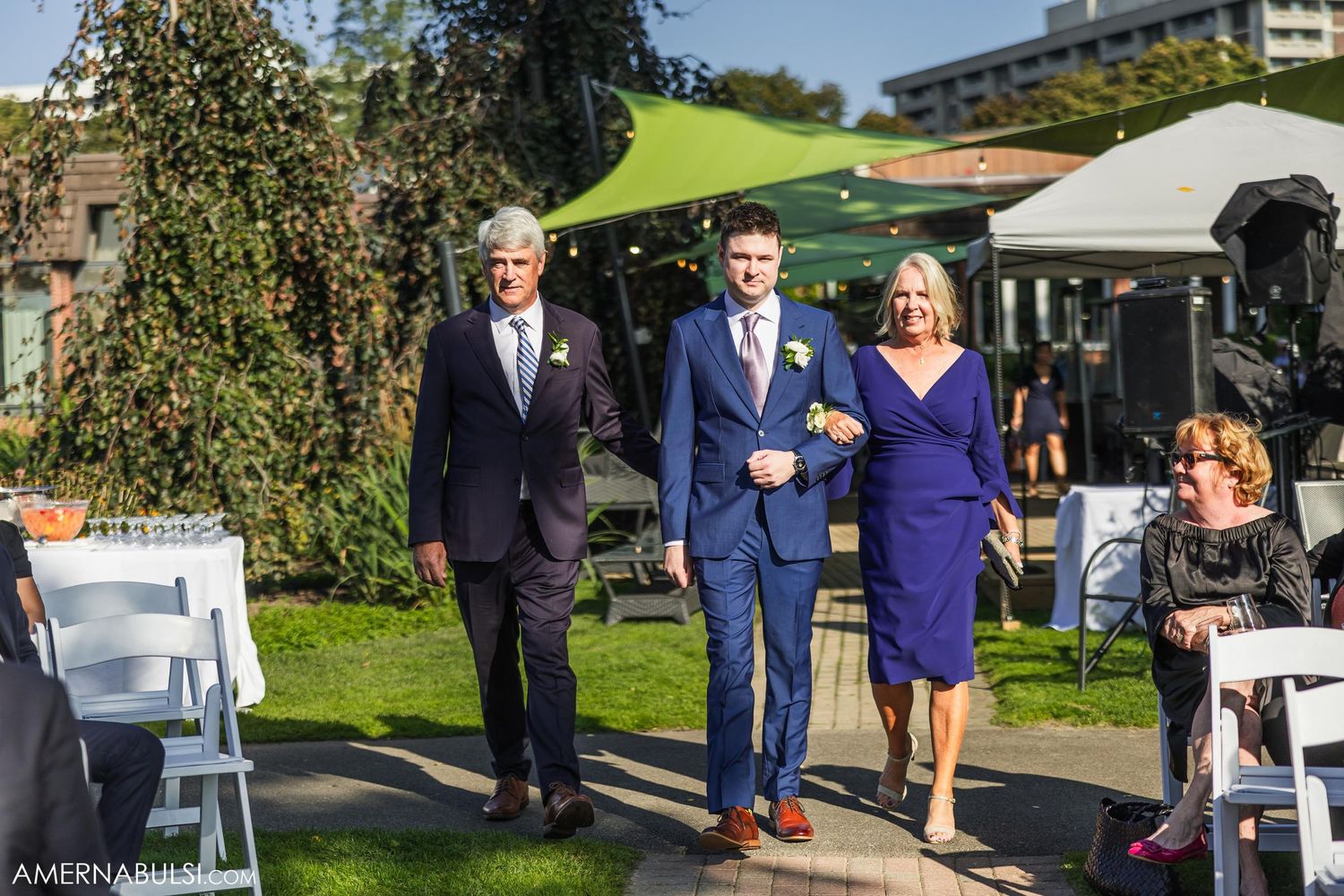 Wedding party walking down outdoor aisle with guests seated under bright blue skies.