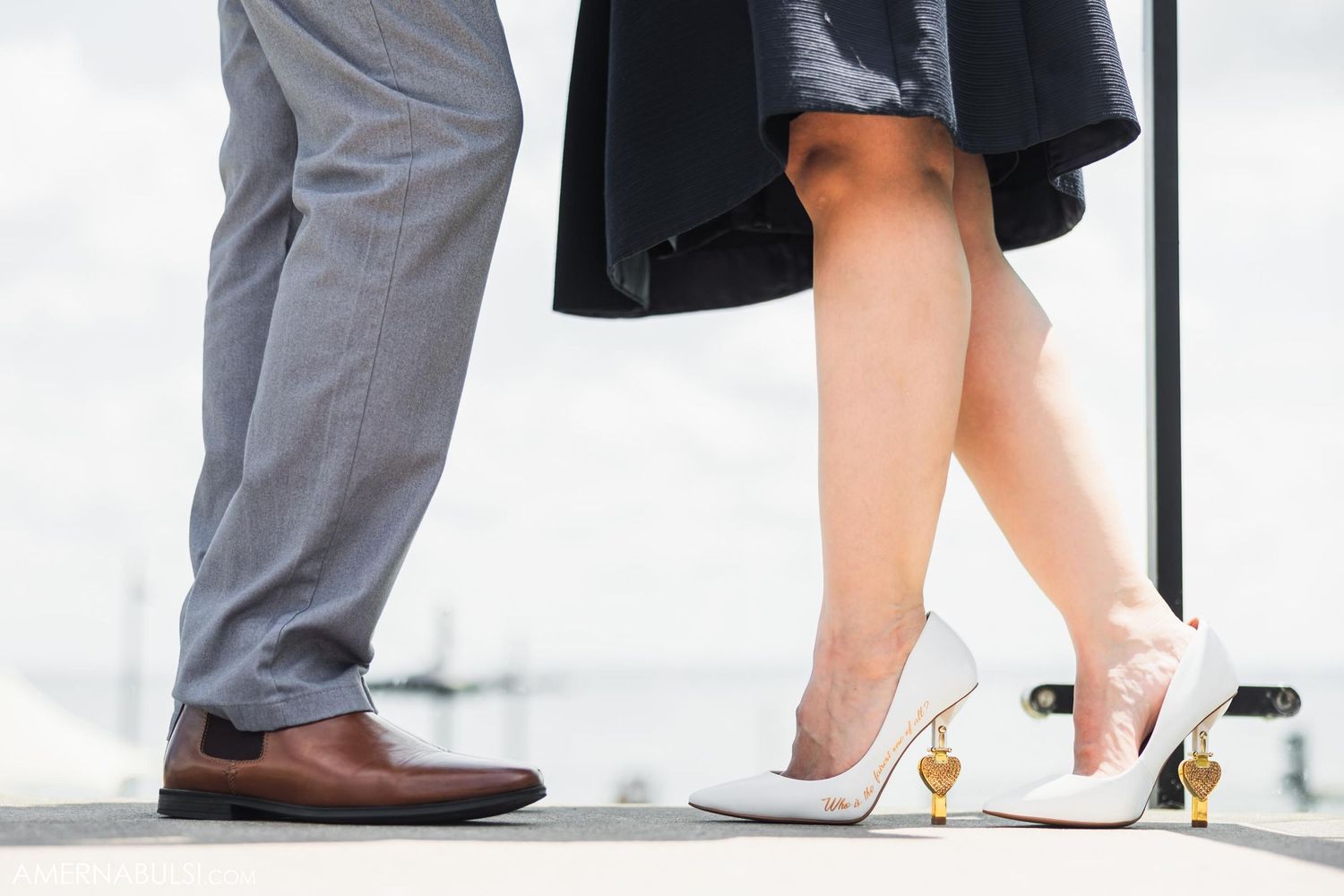 Close-up of feet showing grey dress pants next to a black dress and white heels.