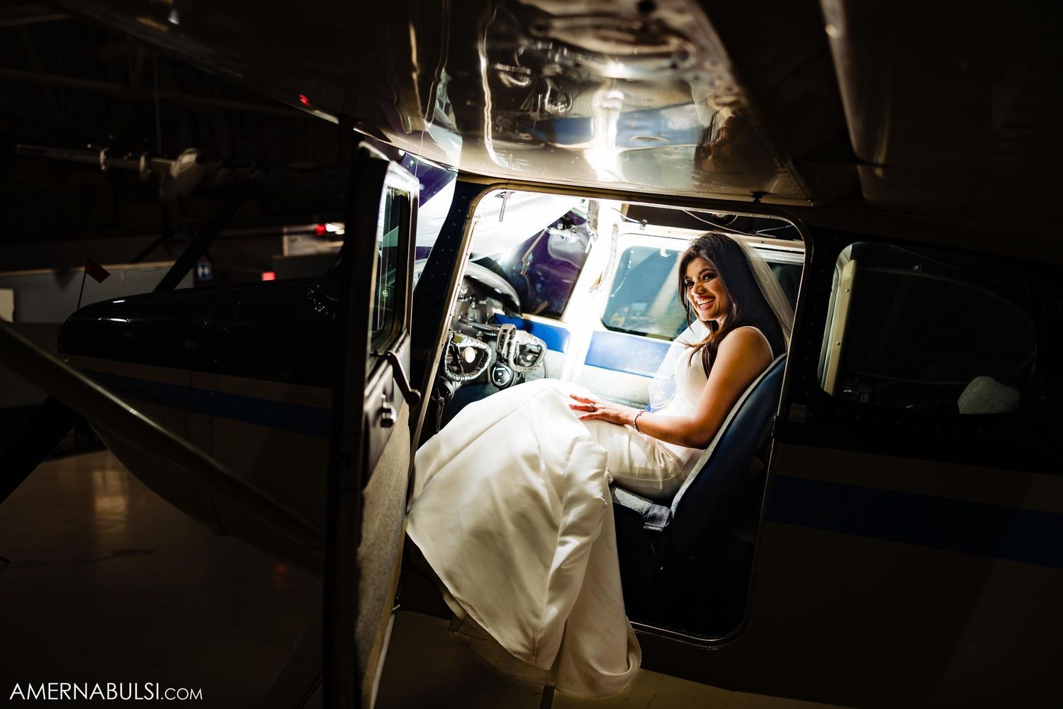 Bride in white dress poses in vintage aircraft interior.
