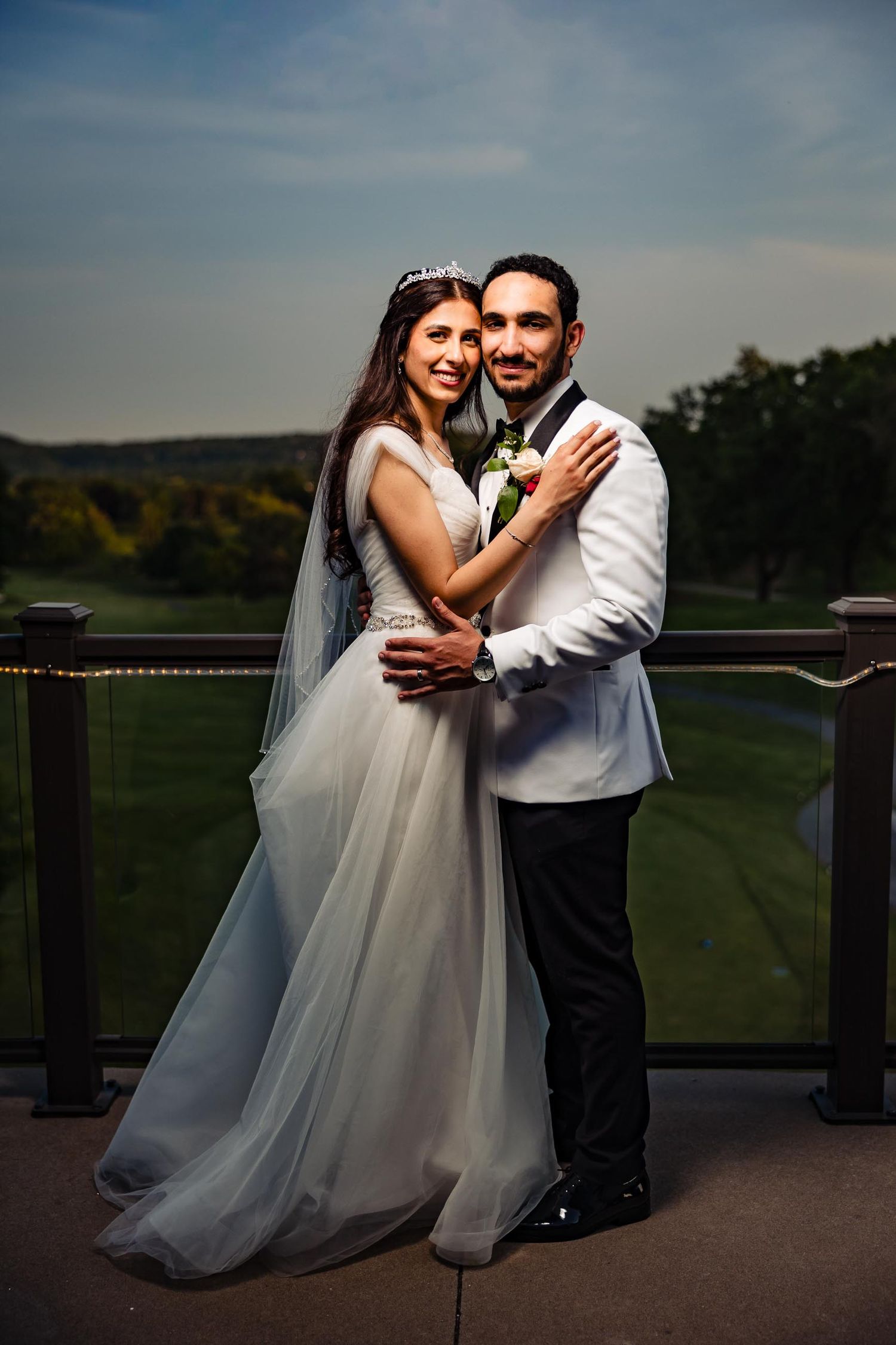 Bride and groom embrace on outdoor terrace with scenic landscape view.