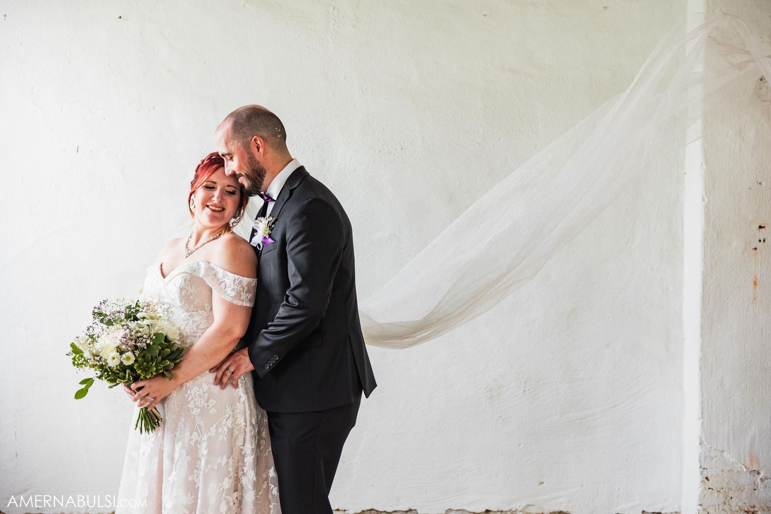 Romantic wedding portrait against white backdrop with flowing veil and white bouquet.