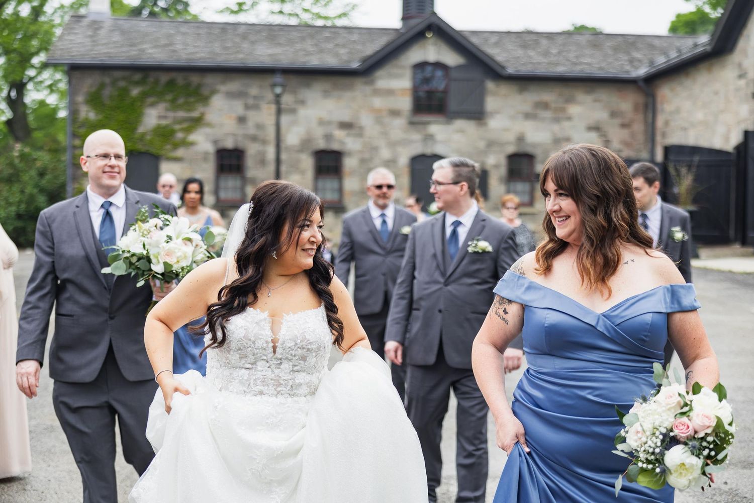 Candid moment of bride with wedding party members on stone courtyard.