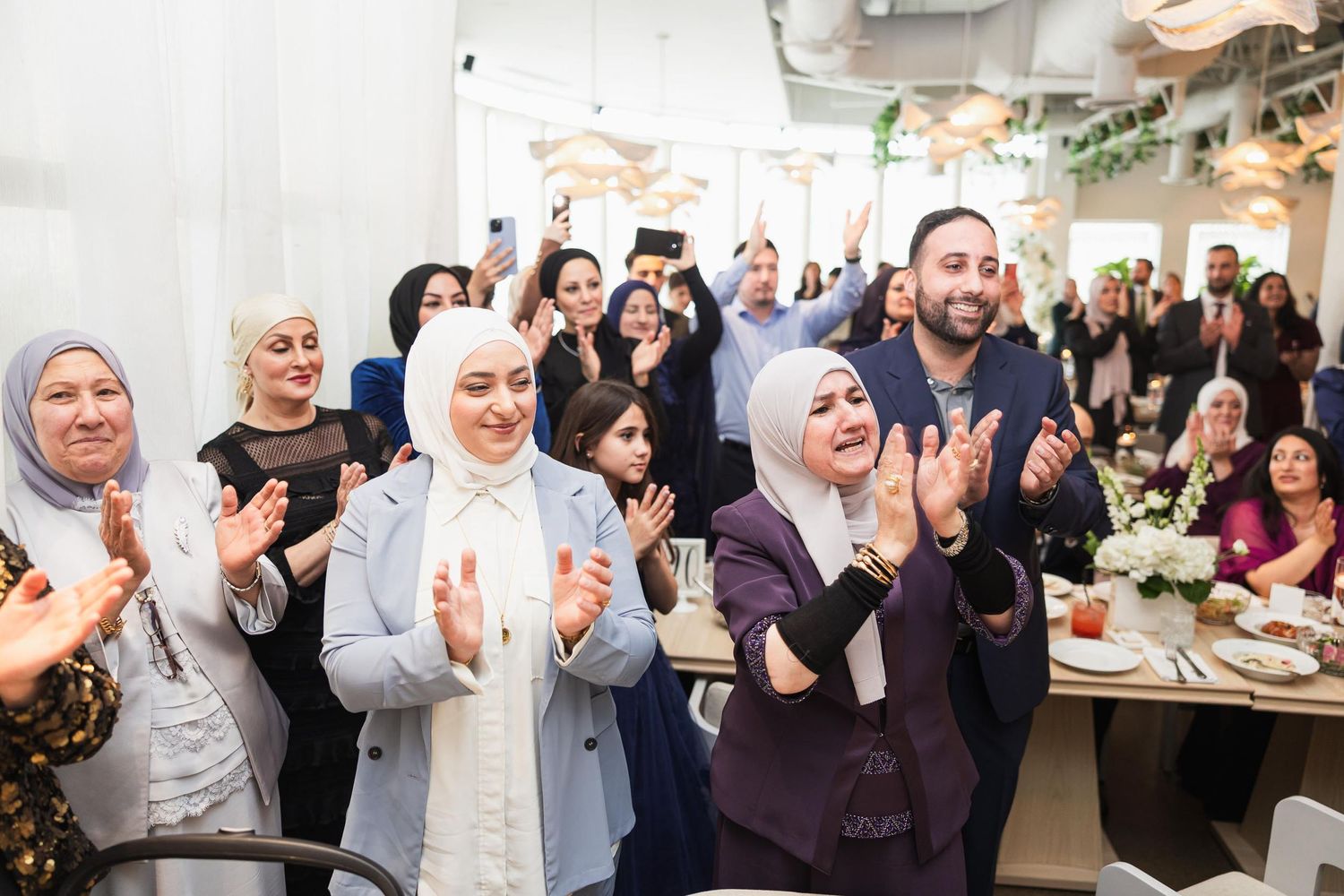 Celebratory crowd clapping and smiling at a modern wedding reception venue.
