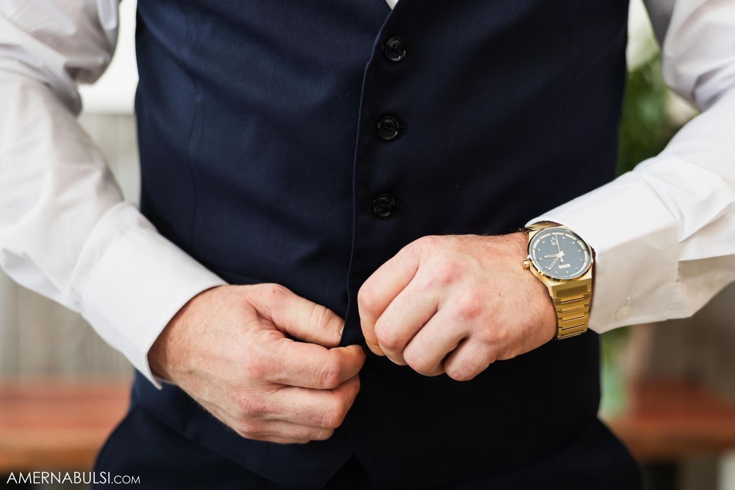 Detail shot of groom adjusting navy vest with elegant watch visible.