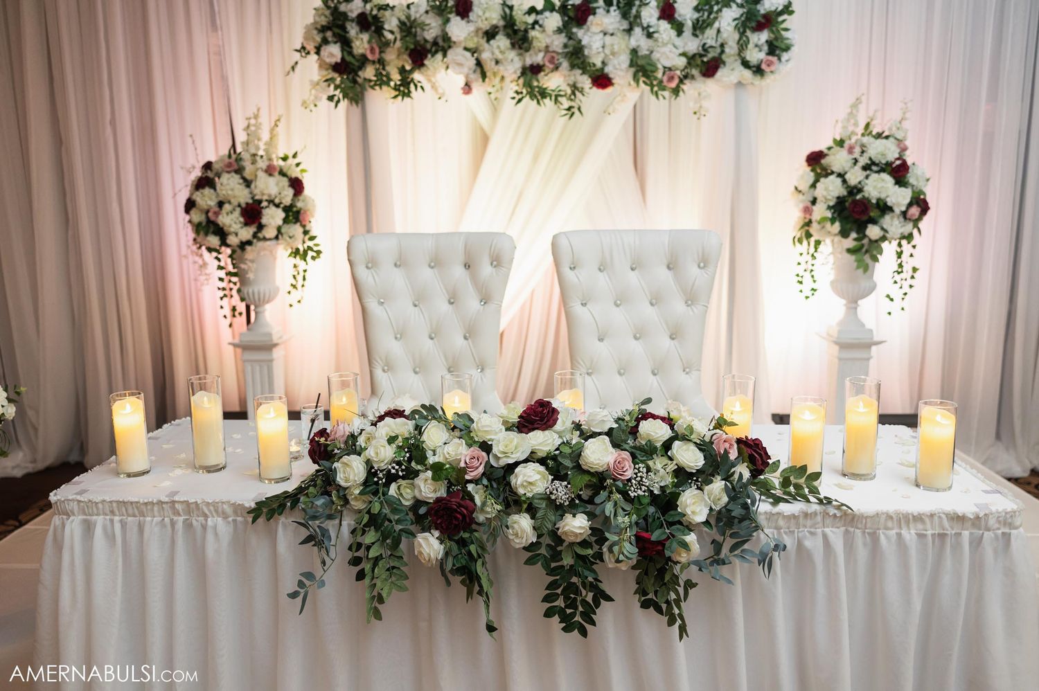 Luxurious sweetheart table with tufted chairs and floral arrangements at wedding reception.