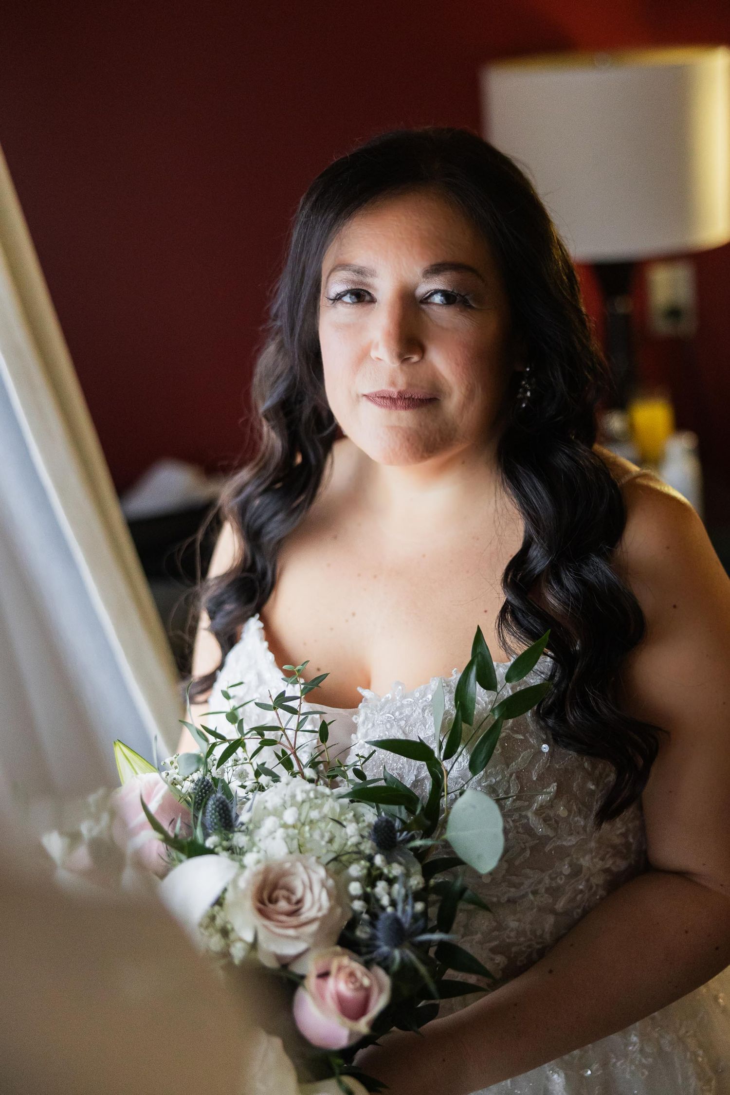 A bride in a white lace dress holds a beautiful bouquet of roses and greenery.