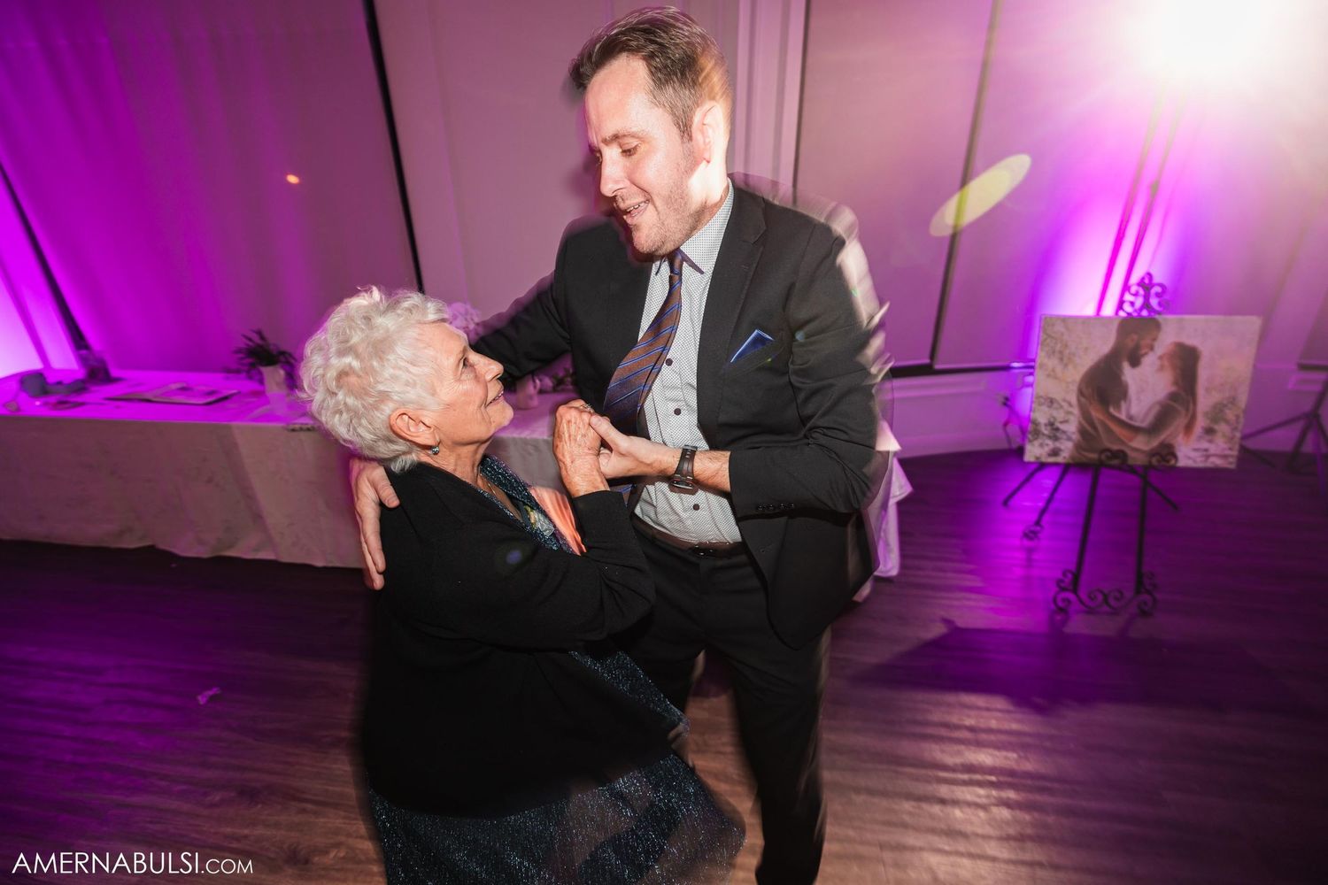 Dancing partners share a joyful moment on the dance floor illuminated by purple lighting at a wedding reception.