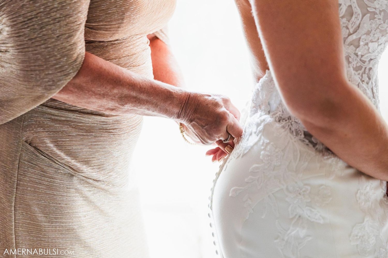 Close up detail of someone helping to lace up the back of an elegant white wedding dress.