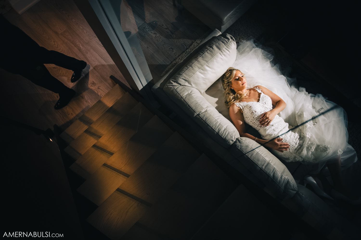 Artistic overhead shot of bride in white gown lying on dark floor.