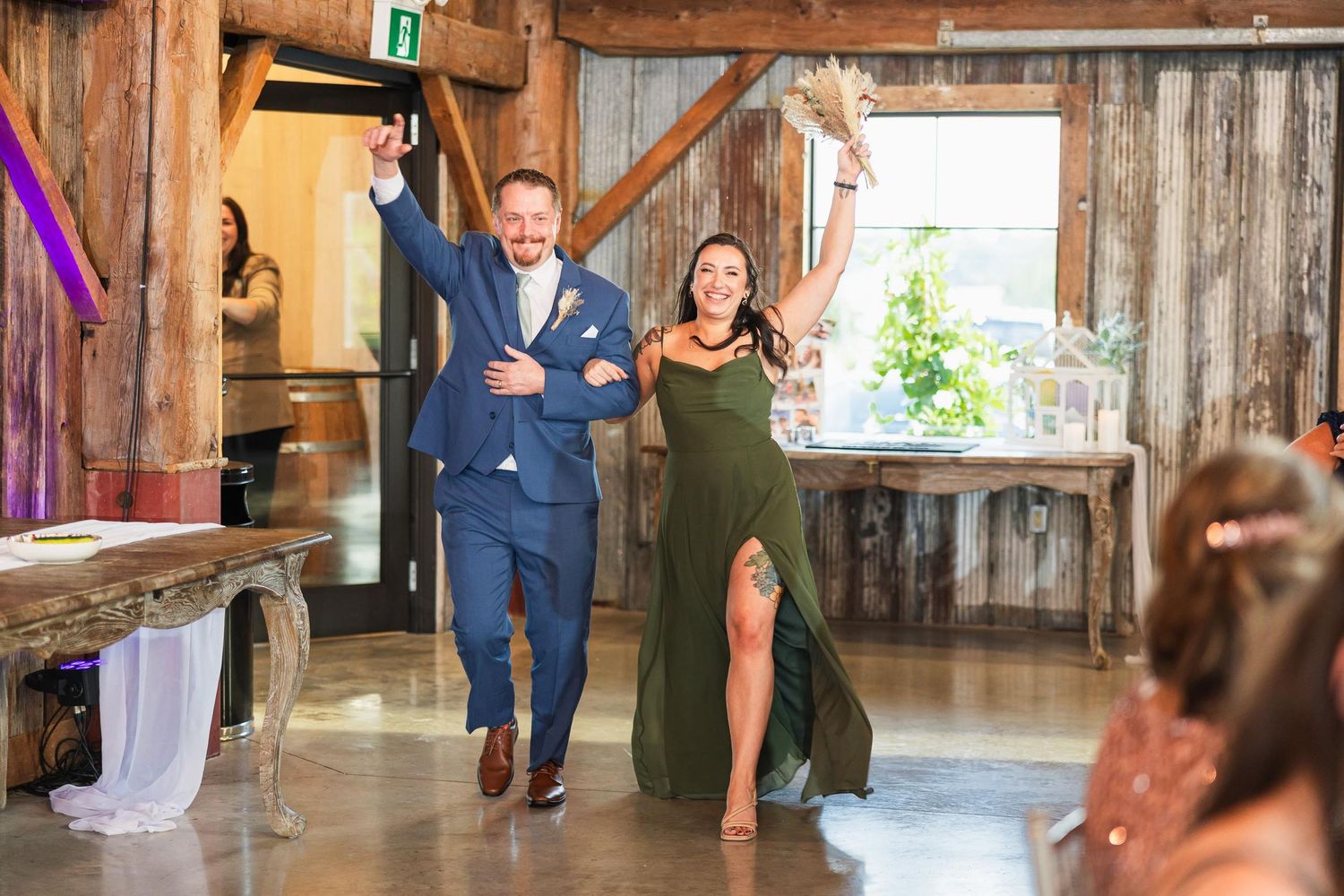 Wedding party pair enters reception venue with arms raised in celebration.