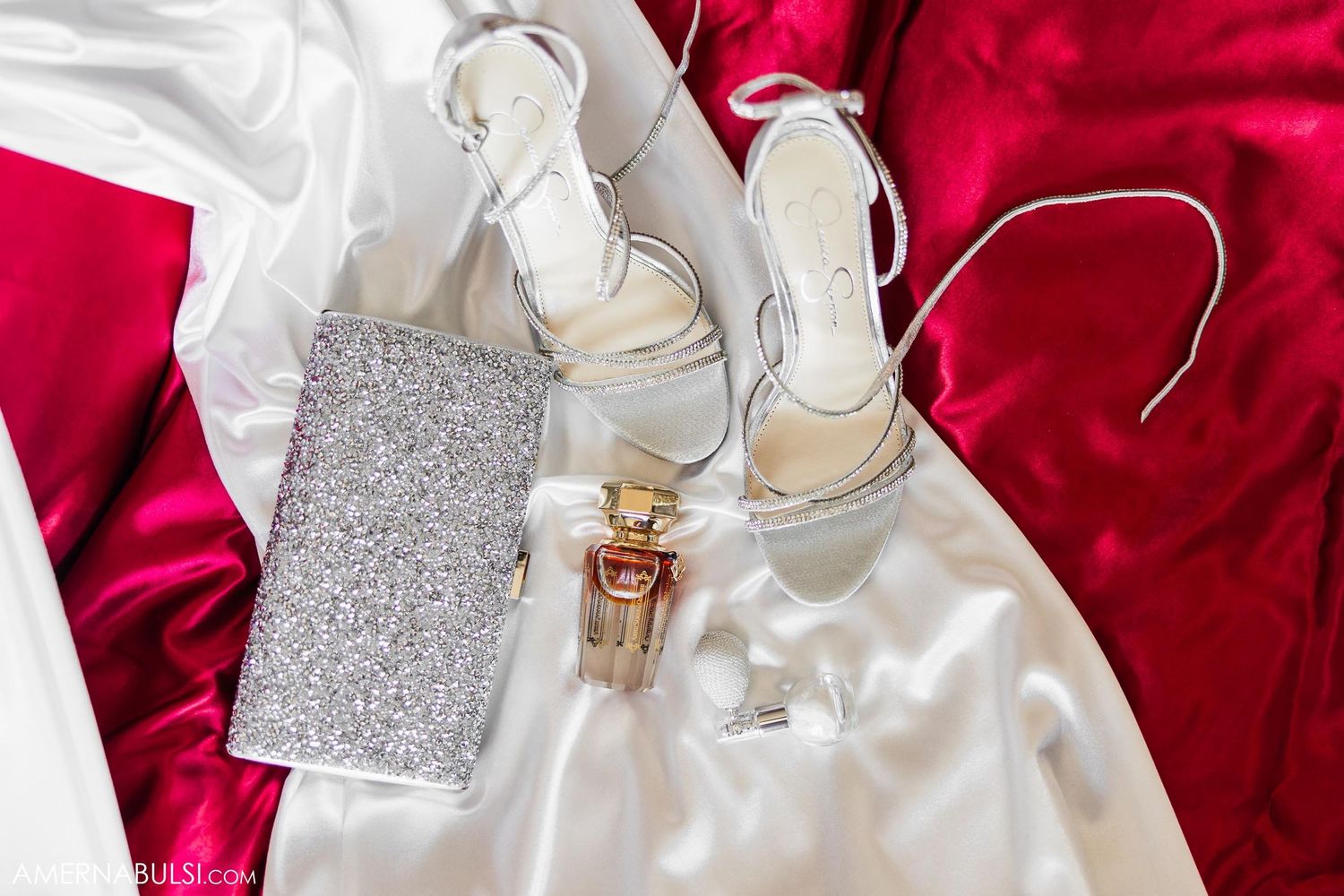 Wedding accessories including silver shoes, a sparkly clutch, and white fabric on red background.