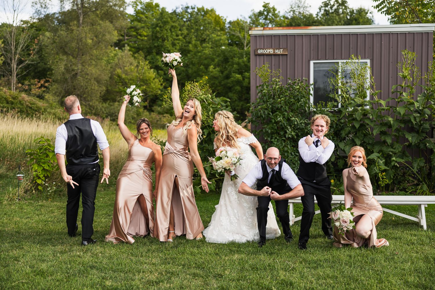 Wedding party posing outdoors in blush pink and formal attire against a natural countryside backdrop.