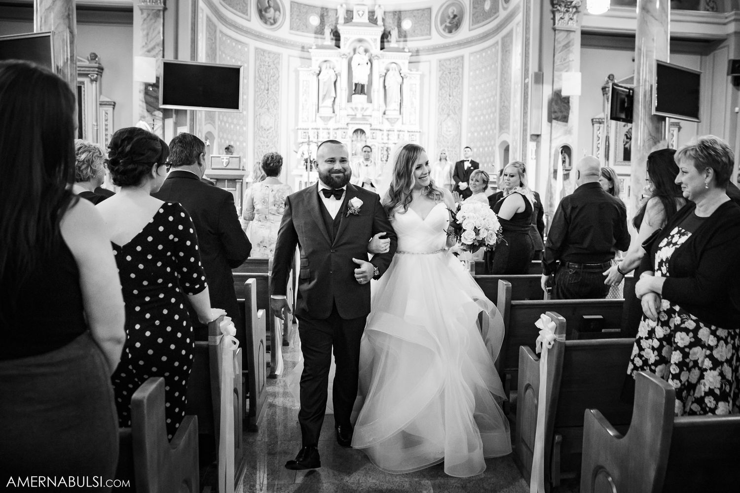 Black and white photo of wedding ceremony inside traditional church with elegant architectural details.